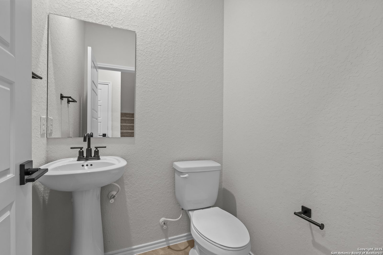 Compact powder room with white pedestal sink, toilet, and mirror in Davidson Homes The Florence C, Cedar Heights, San Antonio, Texas