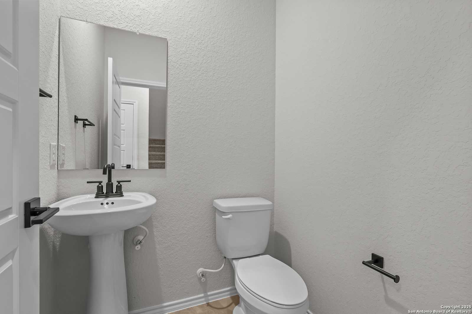 Compact powder room with white pedestal sink, toilet, and mirror in Davidson Homes The Florence C, Cedar Heights, San Antonio, Texas