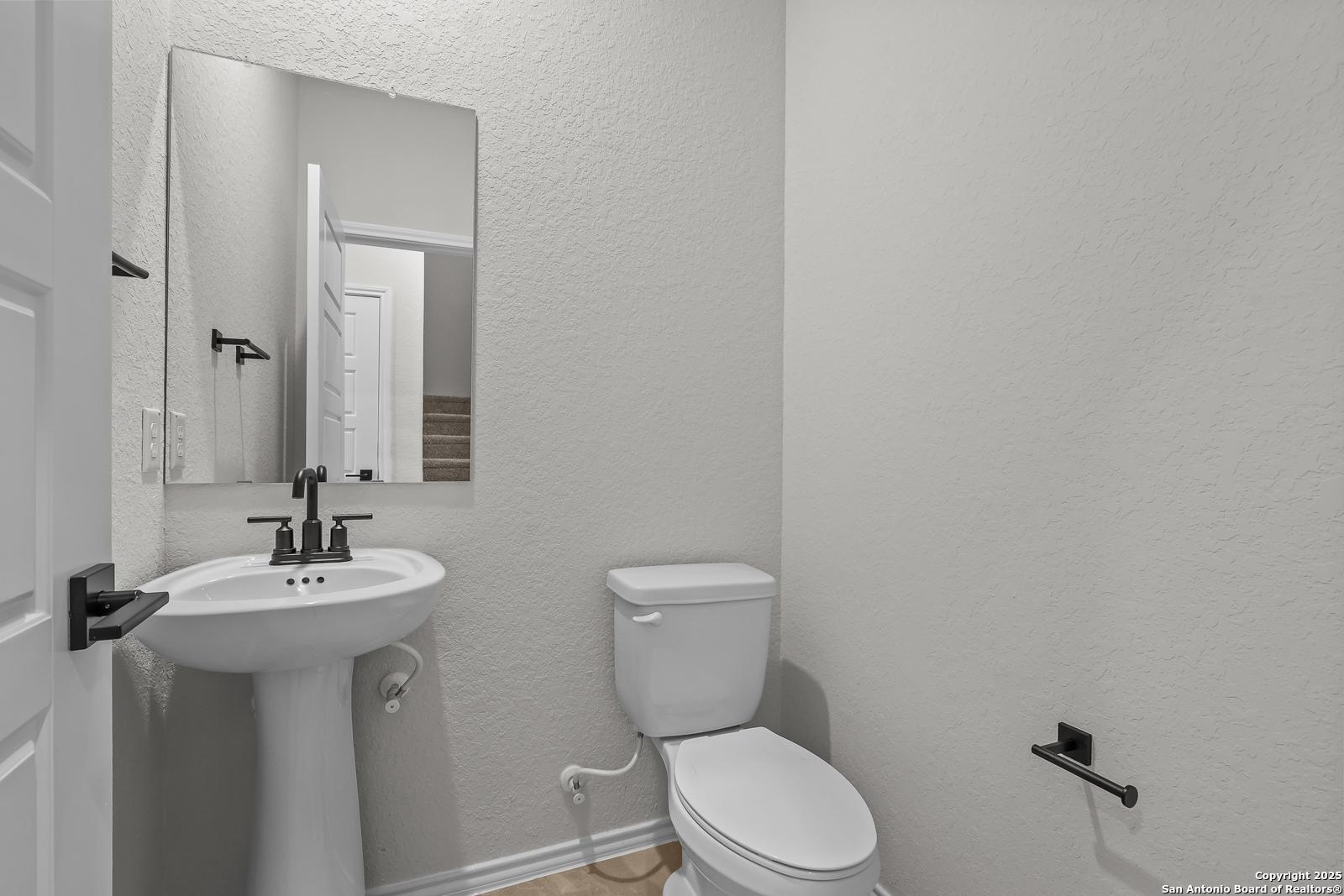 Compact powder room with white pedestal sink, toilet, and mirror in Davidson Homes The Florence C, Cedar Heights, San Antonio, Texas