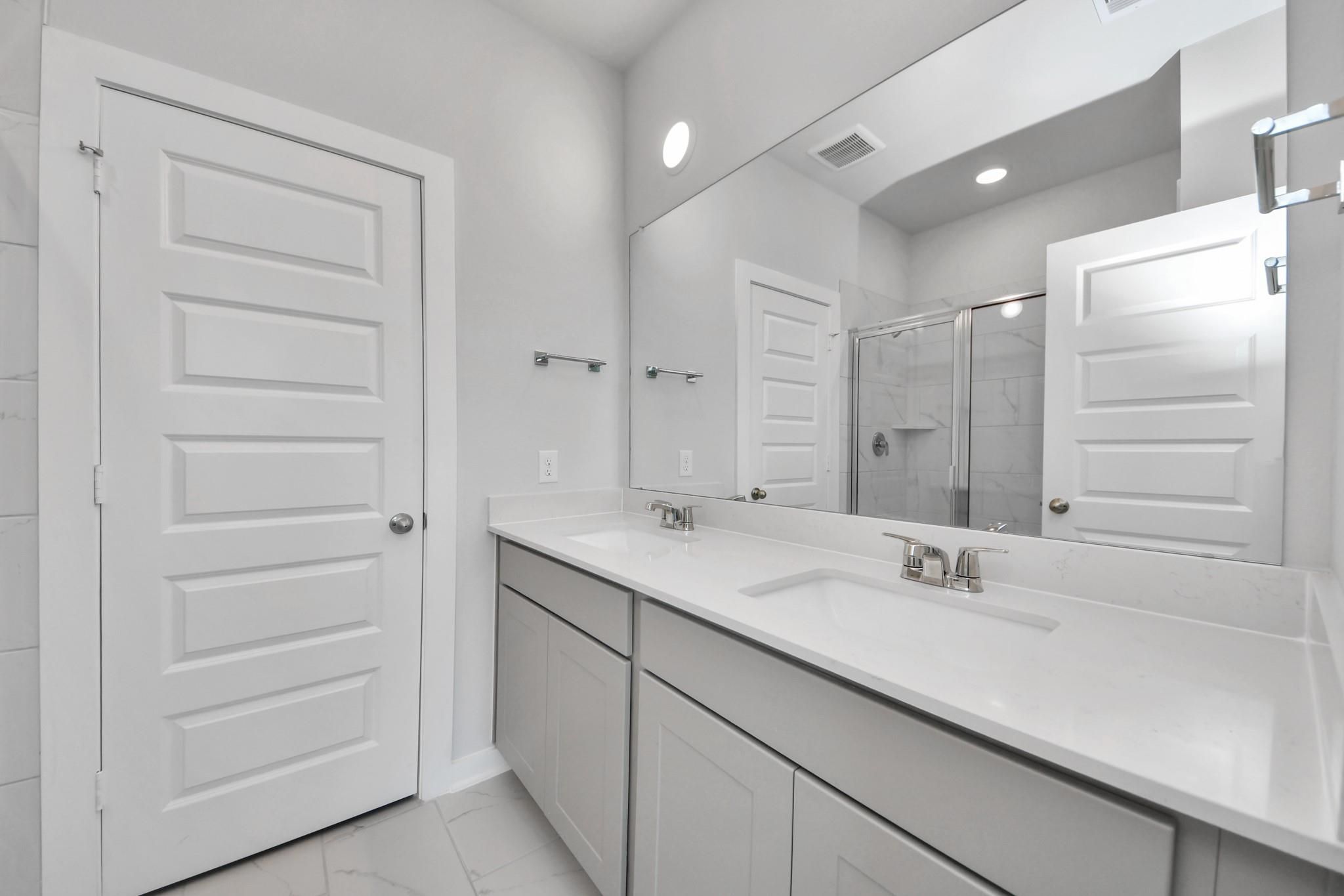 Modern bathroom with dual vanity, quartz countertops, and glass shower in The Colorado G home in Emberly, Beasley, Texas.