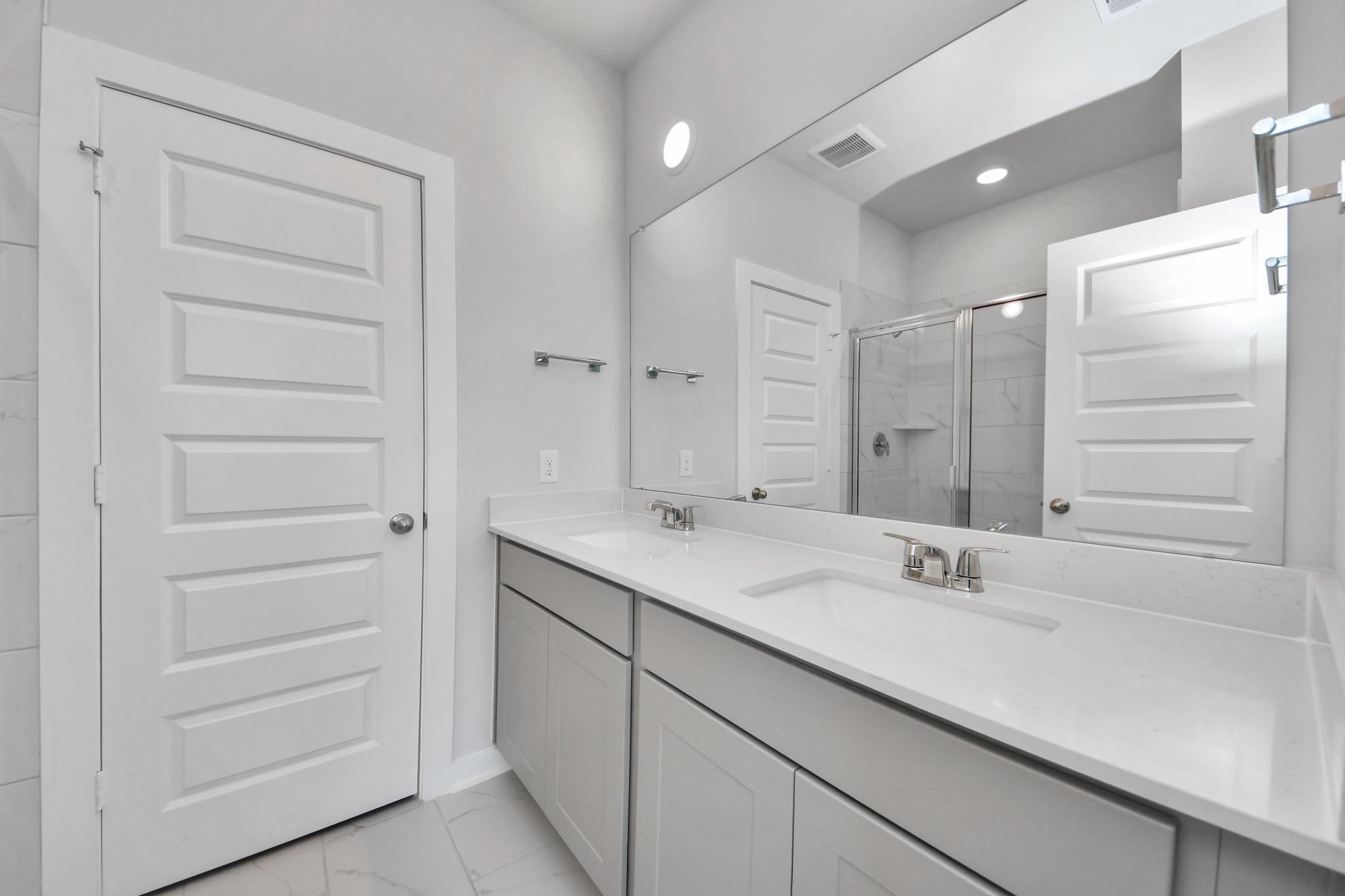 Modern bathroom with dual vanity, quartz countertops, and glass shower in The Colorado G home in Emberly, Beasley, Texas.