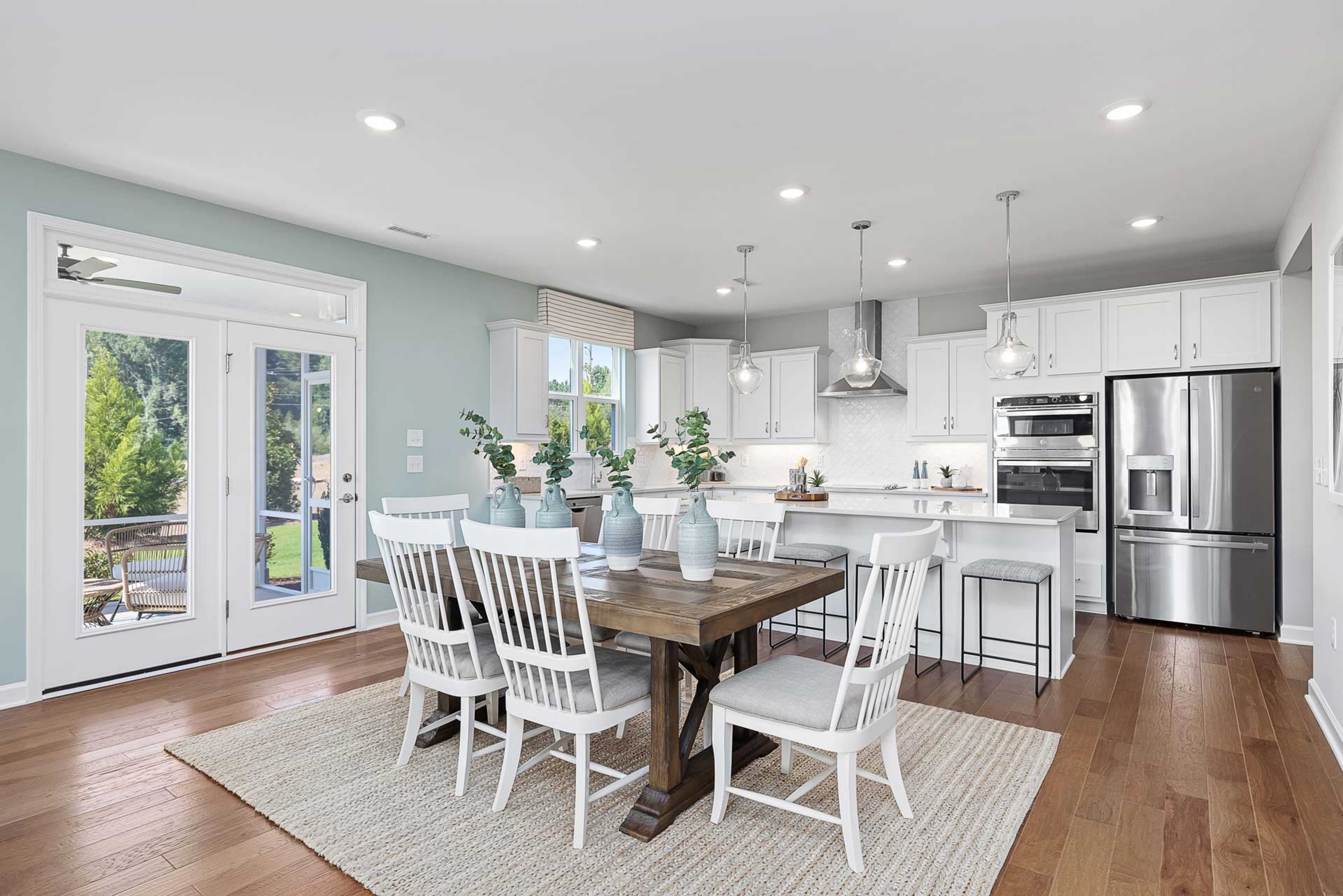 Spacious open-concept kitchen dining area in Highland Forest Fuquay-Varina NC with white cabinets stainless appliances farmhouse table and French doors