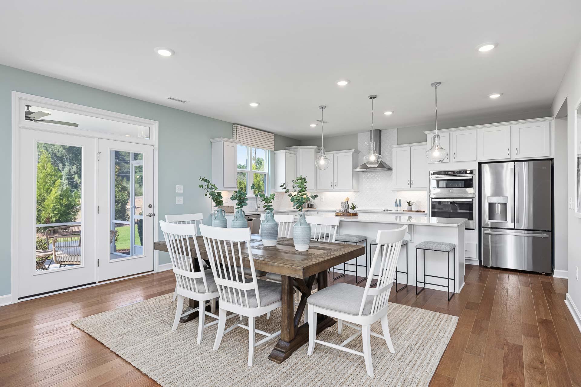 Spacious open-concept kitchen dining area in Highland Forest Fuquay-Varina NC with white cabinets farmhouse table French doors to patio