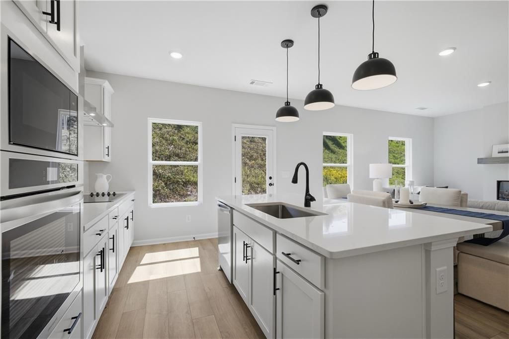 Bright white kitchen with island sink, black pendant lights, and hardwood floors in Davidson Homes Hartwell C, Canton, Georgia