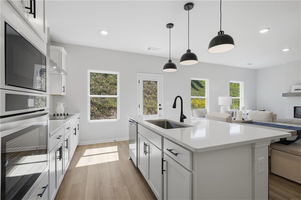 Bright white kitchen with island sink, black pendant lights, and hardwood floors in Davidson Homes Hartwell C, Canton, Georgia