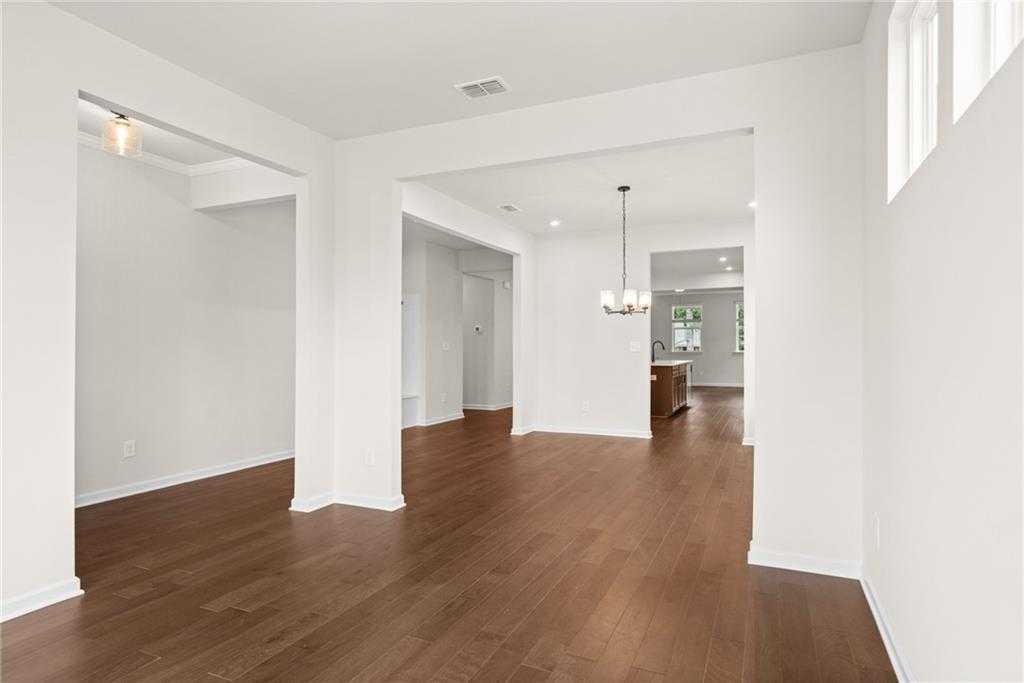 Spacious open-concept living and dining area with hardwood floors, white archways, and chandelier in The Glenwood A, Loganville, GA