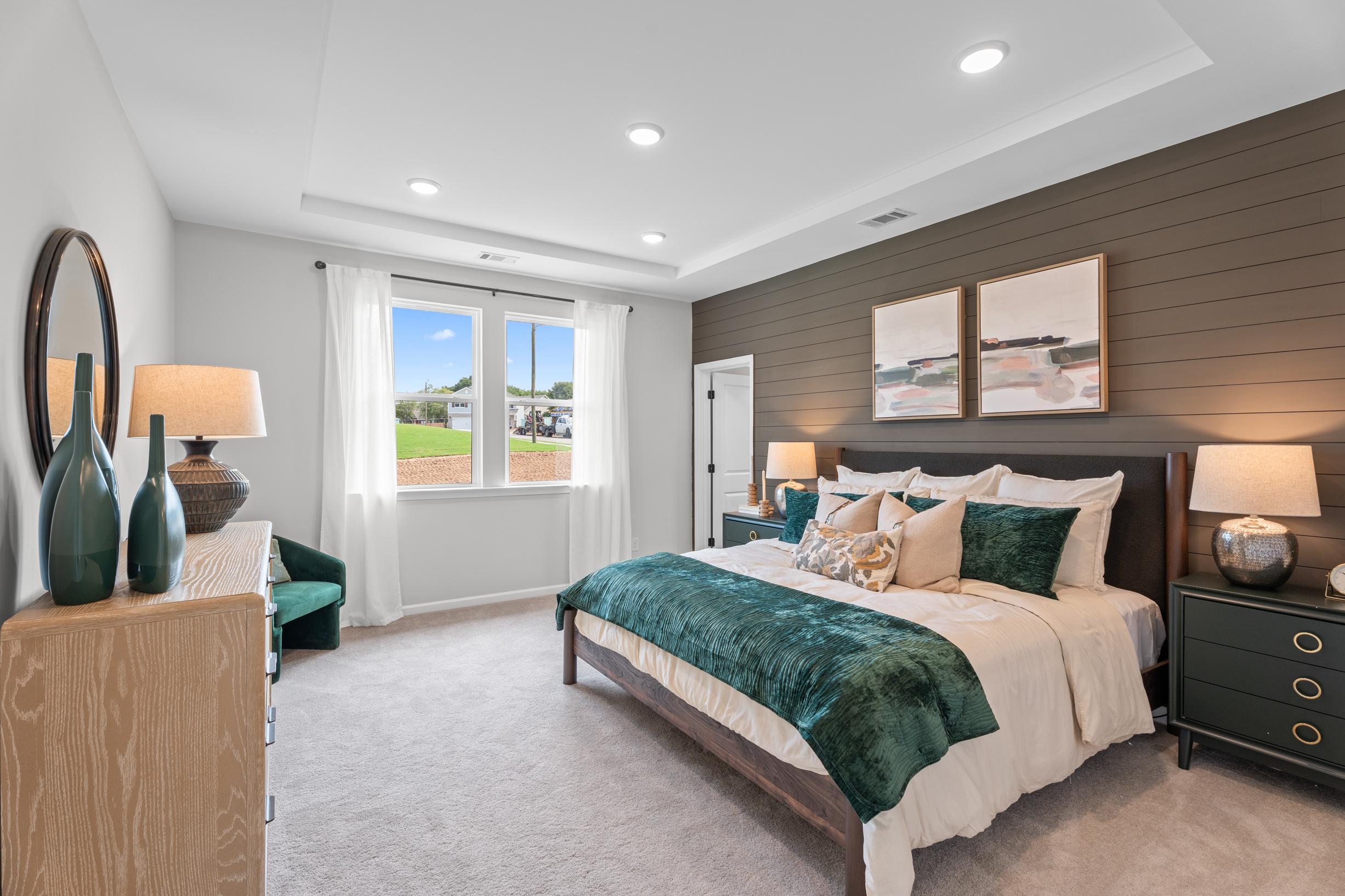 Spacious primary bedroom at Links Crossing in Auburn, AL by Davidson Homes with wood accent wall and green velvet bedding.