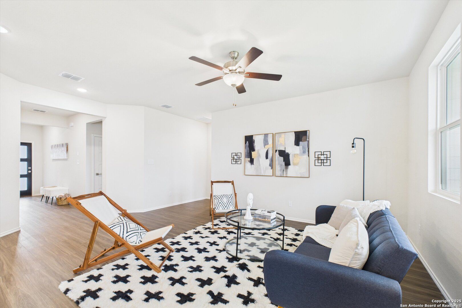 Modern living room featuring navy blue sofa, patterned rug, armchairs, abstract art, and ceiling fan in Davidson Homes The Asheville K, Bricewood San Antonio
