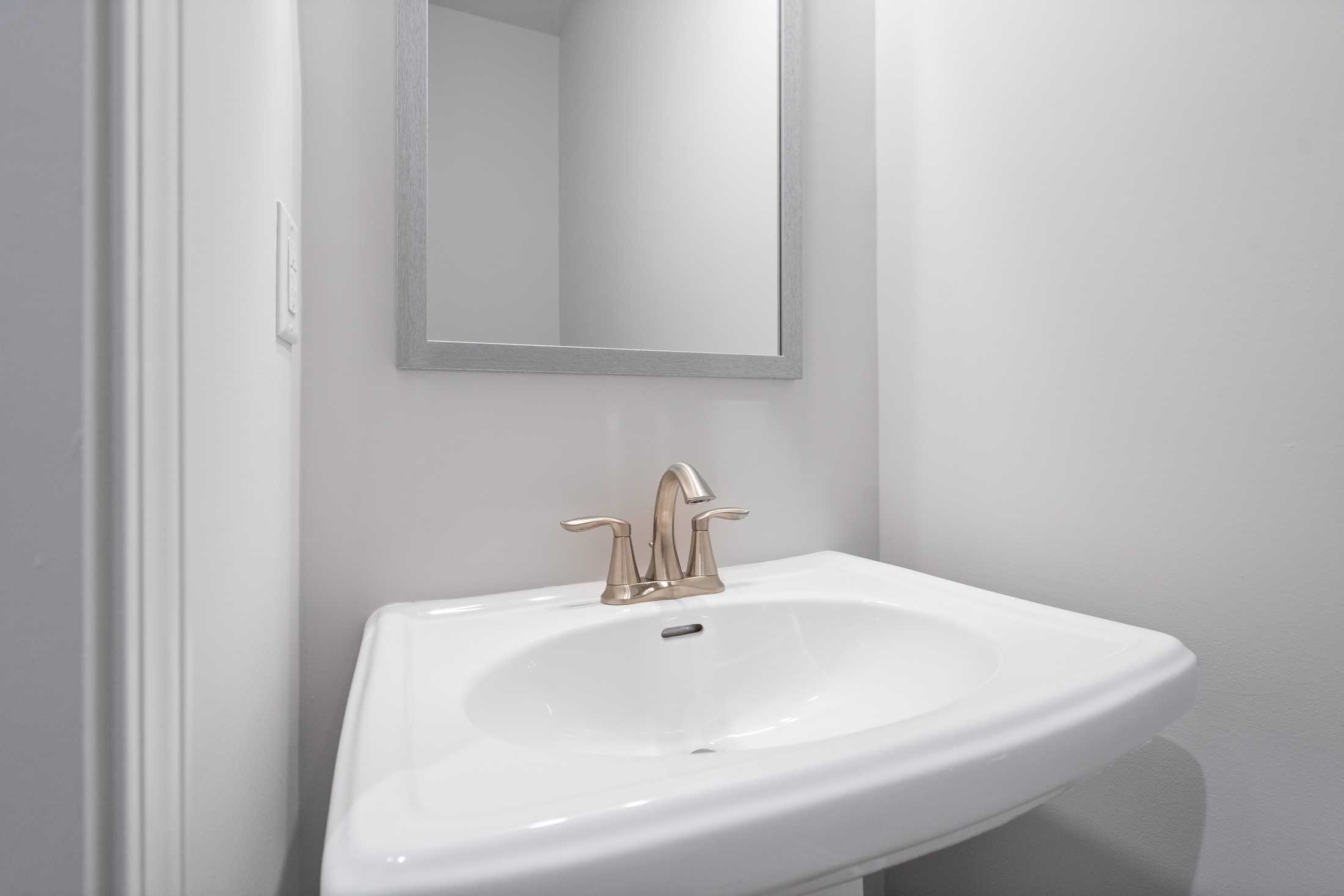 The Cary A powder room vanity with white pedestal sink, brushed gold faucet, and framed mirror in Davidson Homes design