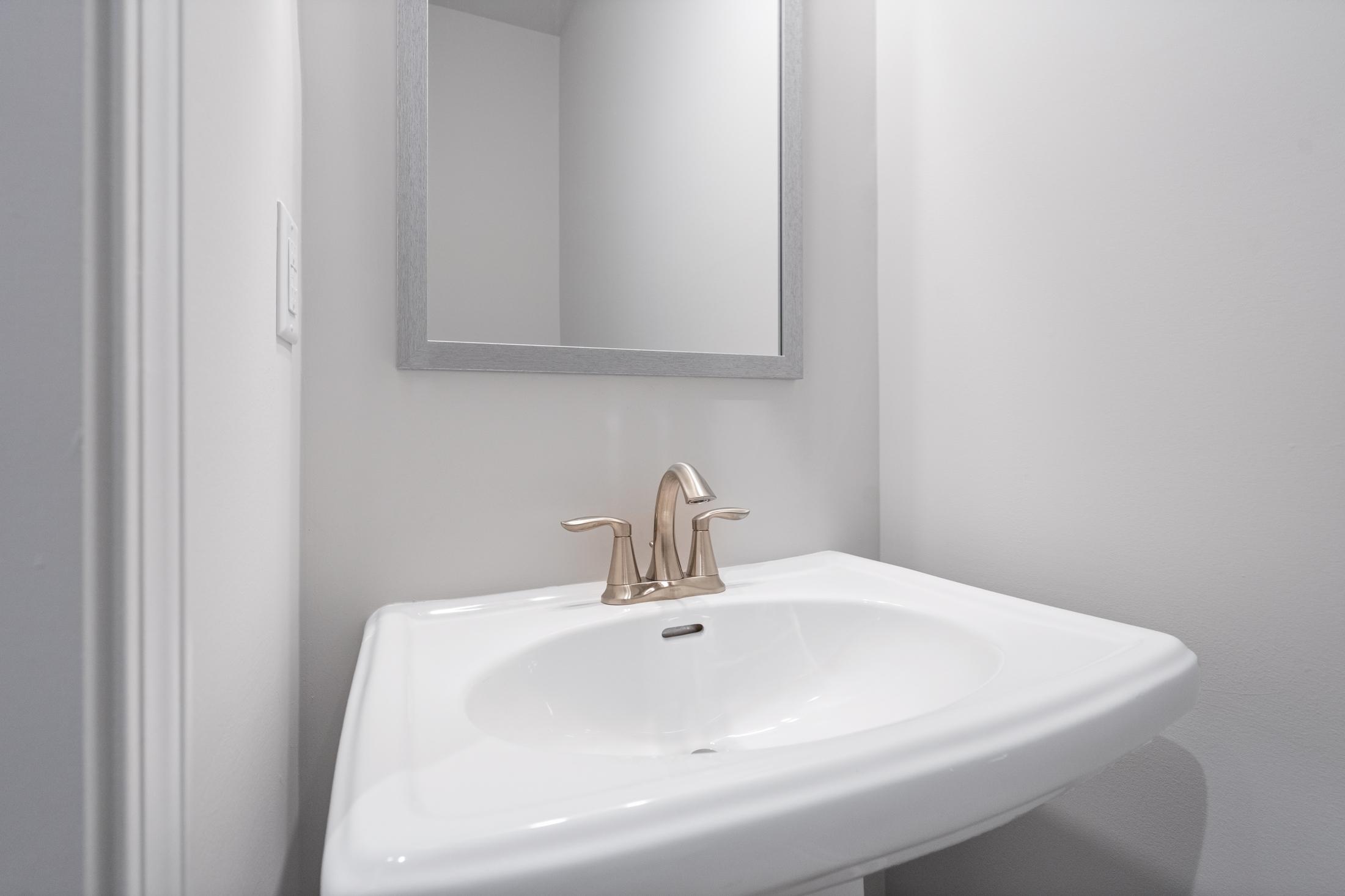 The Cary A powder room vanity with white pedestal sink, brushed gold faucet, and framed mirror in Davidson Homes design