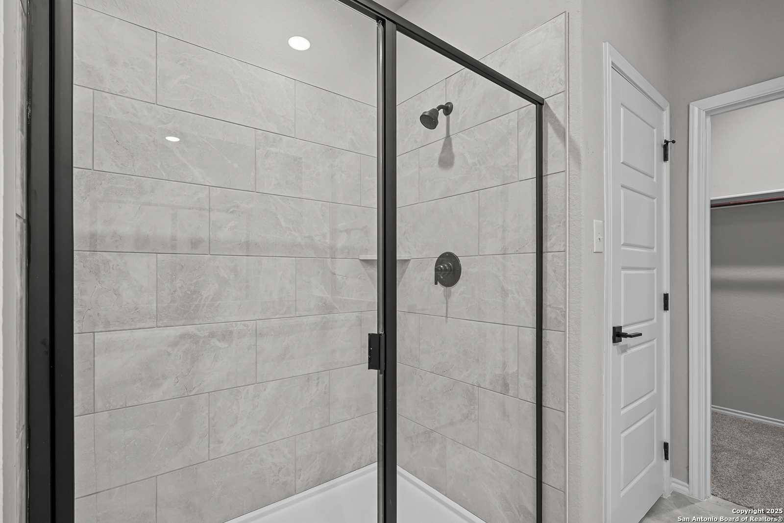 Modern frameless glass shower with gray subway tiles, rainfall showerhead, and black fixtures in The Daphne K master bath, San Antonio