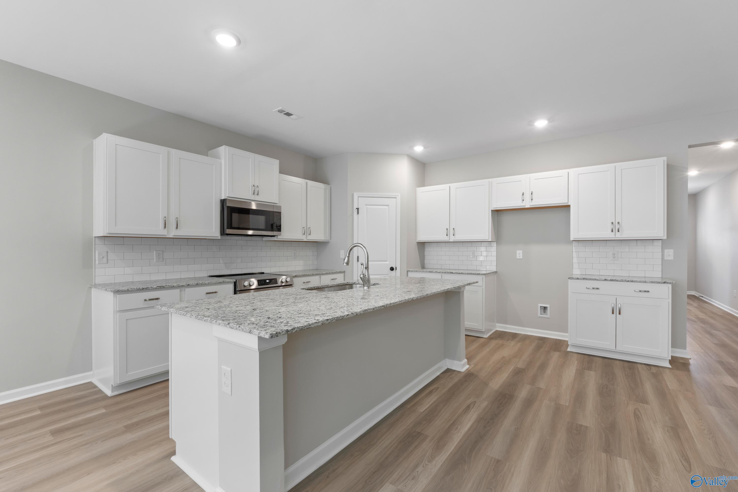 Modern white kitchen featuring granite island, stainless appliances, subway tile backsplash in Davidson Homes The Phoenix, Fayetteville, TN
