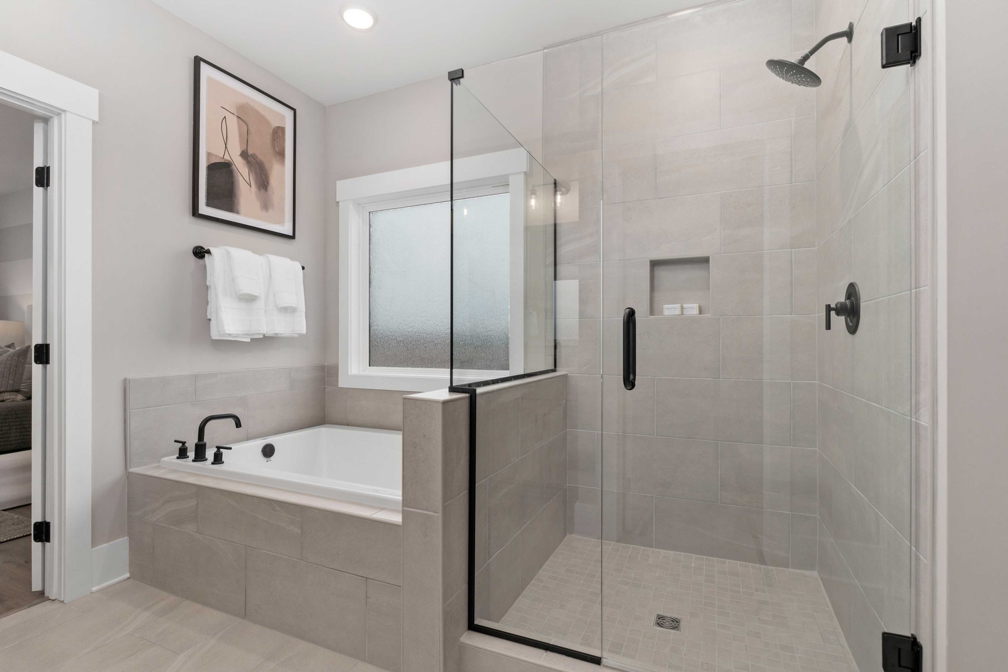 Modern master bathroom at Kendall Farms in Toney, Alabama featuring frameless glass shower and soaking tub with neutral tiles