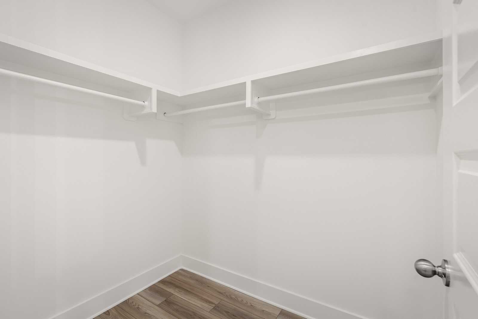 Spacious walk-in closet with white built-in shelves, hanging rods, and hardwood floors in Davidson Homes The Hathaway, Murfreesboro