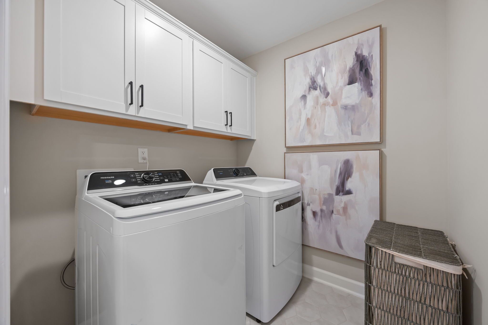 Modern laundry room at Forestville Yard Townhomes in Knightdale NC with white Frigidaire washer dryer cabinets and abstract art