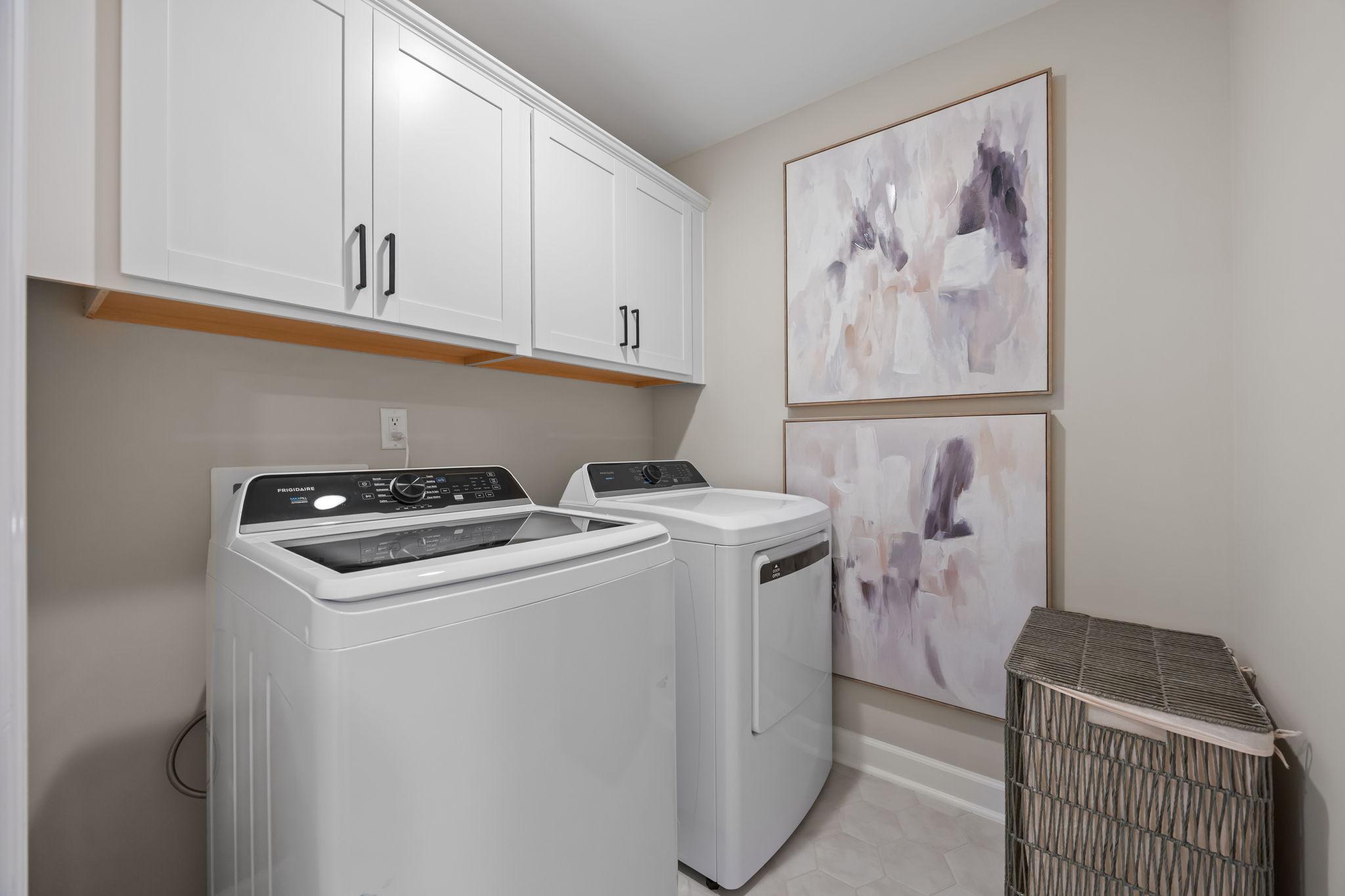 Modern laundry room at Forestville Yard Townhomes in Knightdale NC with white Frigidaire washer dryer cabinets and abstract art