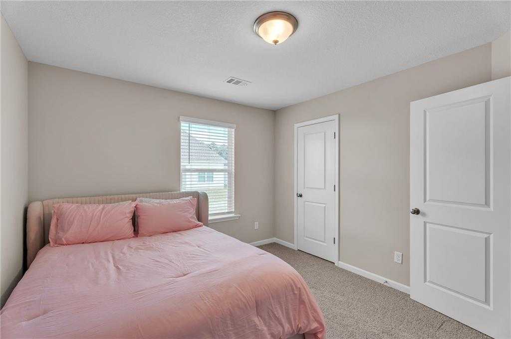 Cozy bedroom with pink bedding on queen bed, beige walls, window blinds in Davidson Homes The Bartlett, Phenix City, Alabama