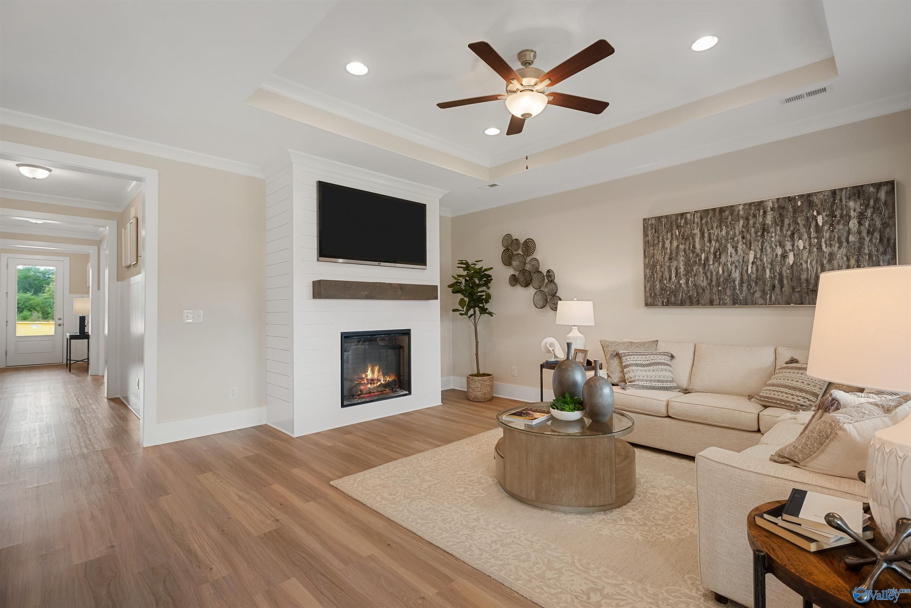 Cozy living room with gas fireplace, mounted TV, beige sofa, ceiling fan in Davidson Homes The Everett, New Market, Alabama