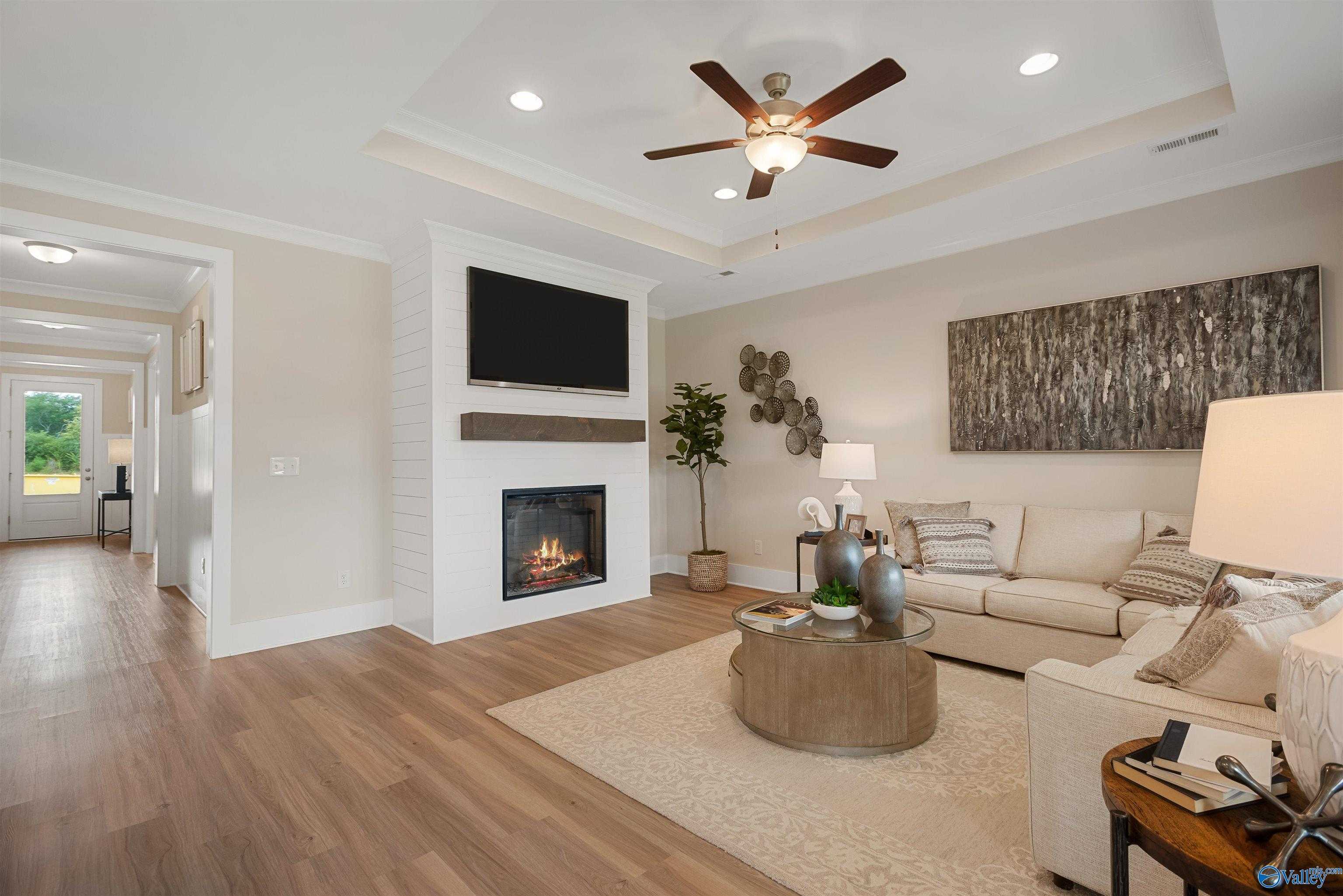 Cozy living room with gas fireplace, mounted TV, beige sofa, ceiling fan in Davidson Homes The Everett, New Market, Alabama