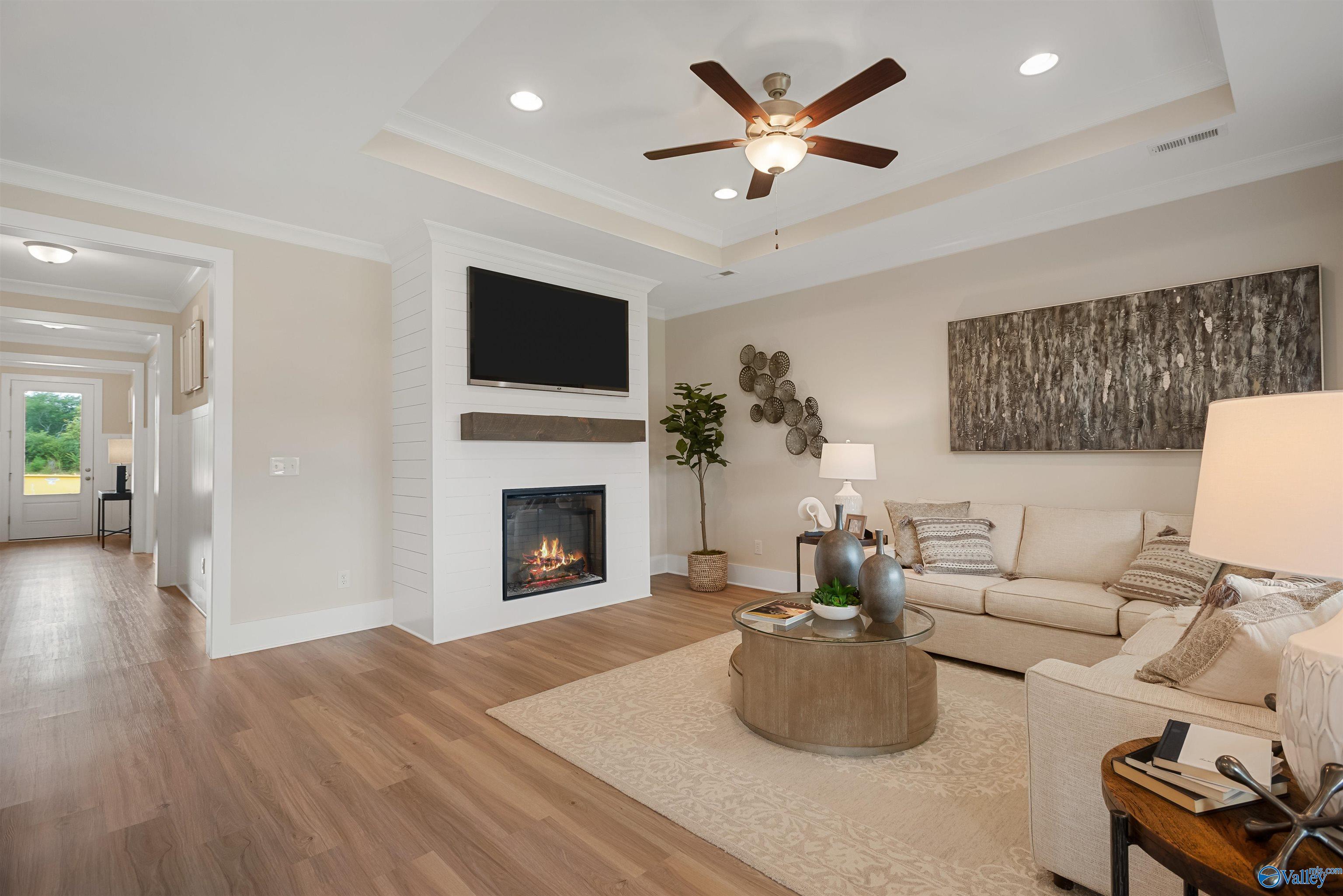 Cozy living room with gas fireplace, mounted TV, beige sofa, ceiling fan in Davidson Homes The Everett, New Market, Alabama