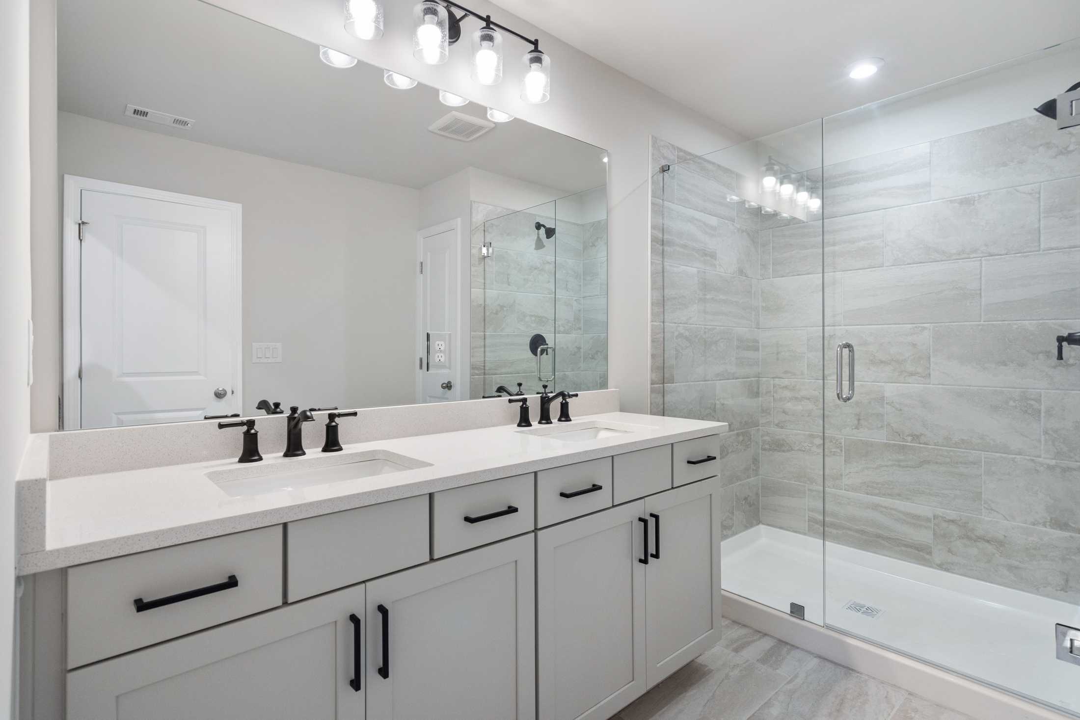 Modern master bathroom in The Cary B featuring double vanity, subway tile shower, and sleek lighting