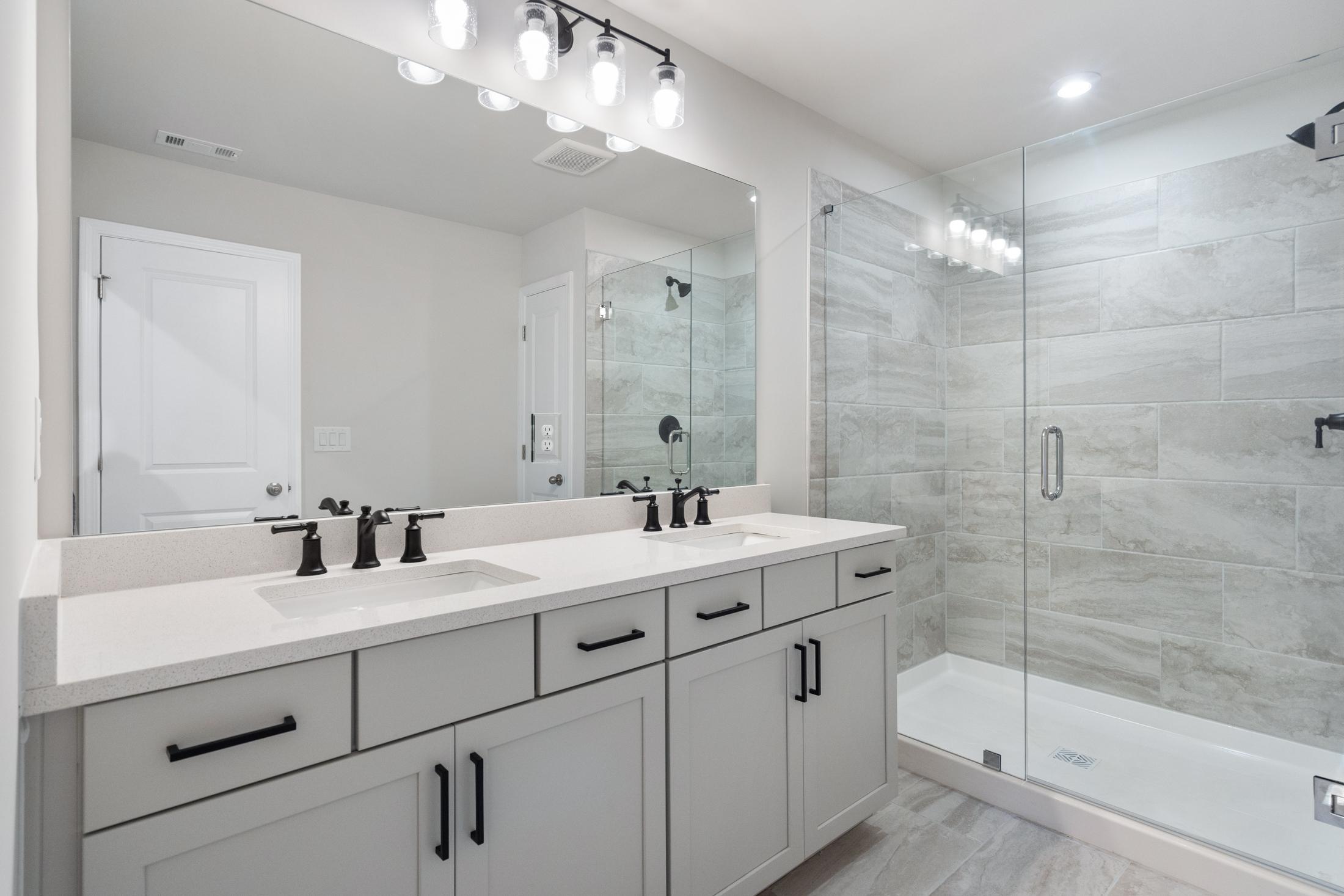 Modern master bathroom in The Cary B featuring double vanity, subway tile shower, and sleek lighting