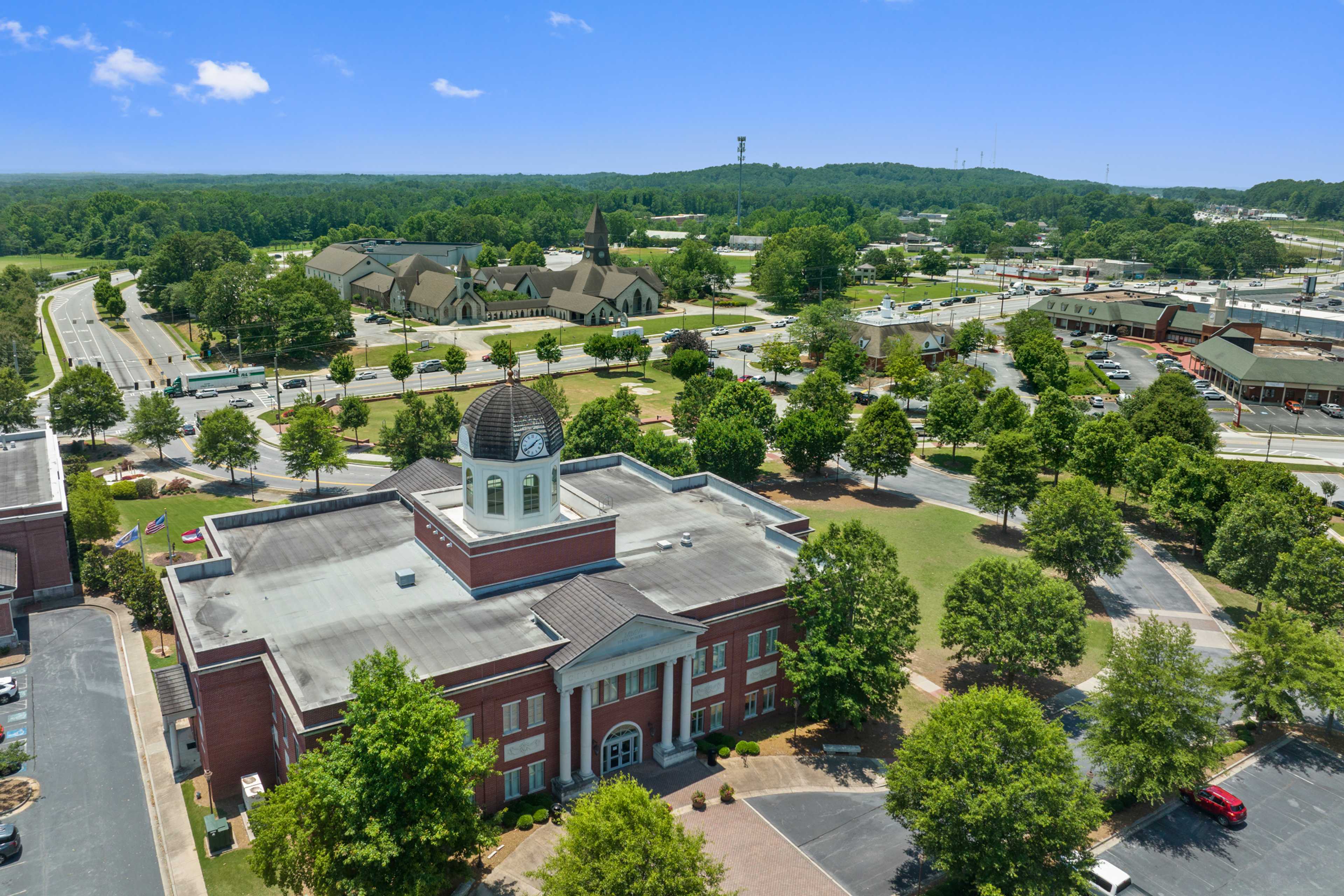 Aerial view of historic red brick courthouse with clock tower in Loganville Georgia near Kelly Preserve featuring green lawns trees and parking