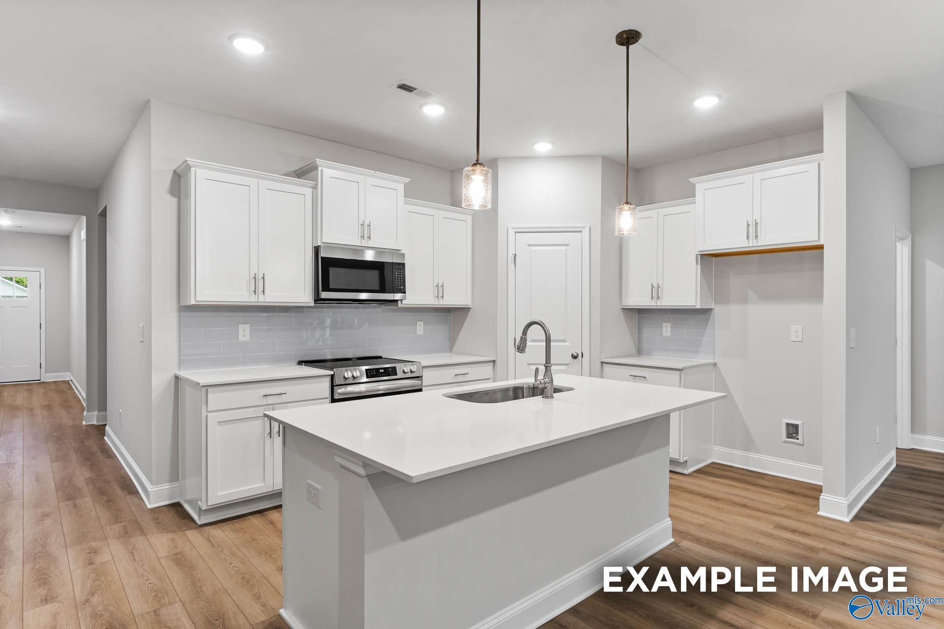 Modern white kitchen with quartz island, stainless appliances, and open layout in The Daphne 4-bedroom home by Davidson Homes, Meridianville, AL