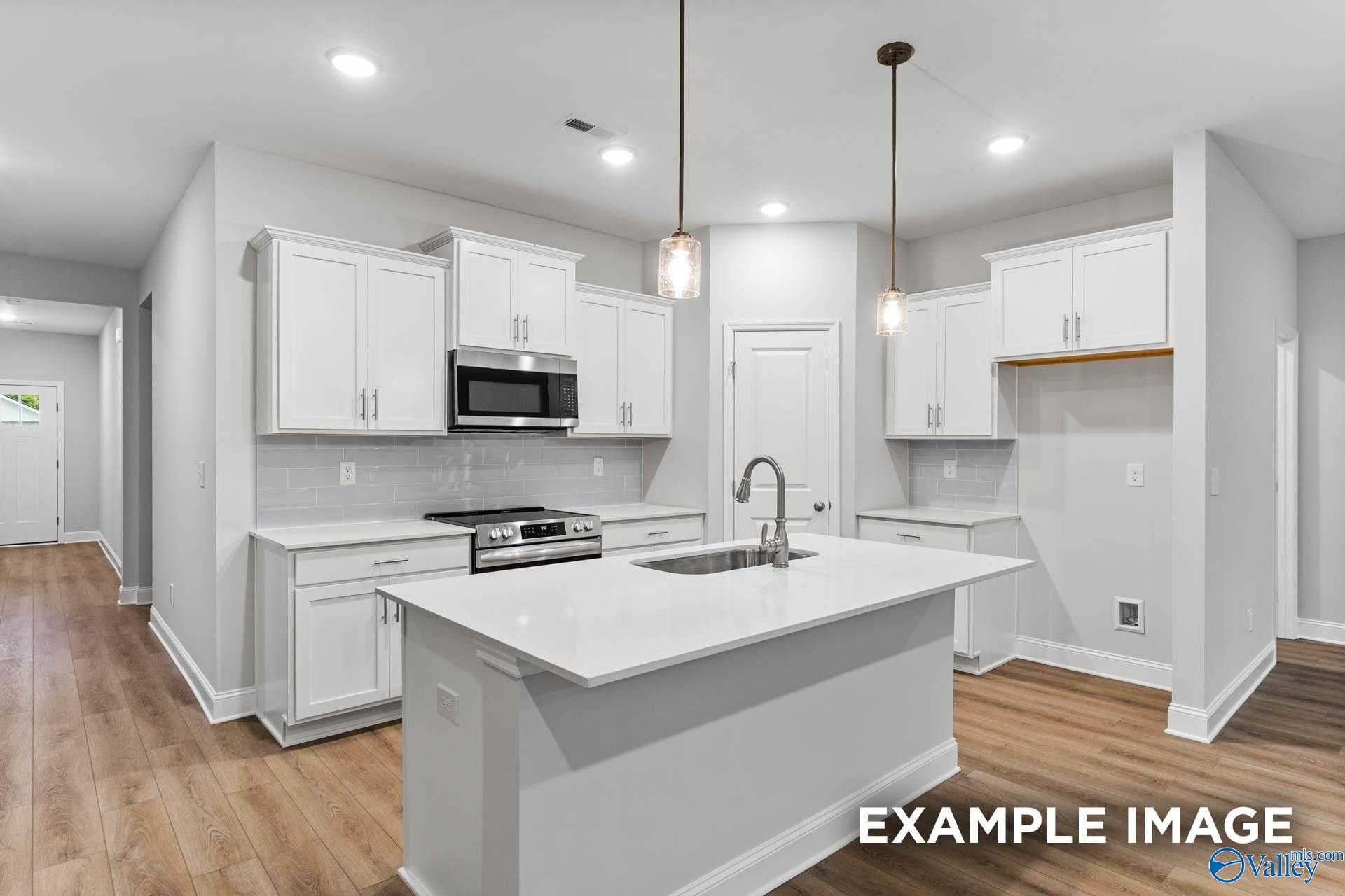 Modern white kitchen with stainless appliances, quartz island, and open layout in The Daphne 4-bedroom home, Meridianville, Alabama