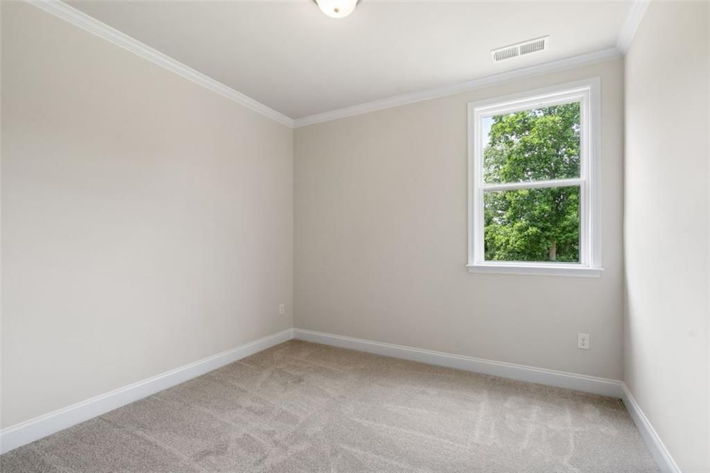 Bright empty secondary bedroom with beige walls, carpet floor, and window overlooking trees in Davidson Homes The Willow D at Wehunt Meadows, Hoschton