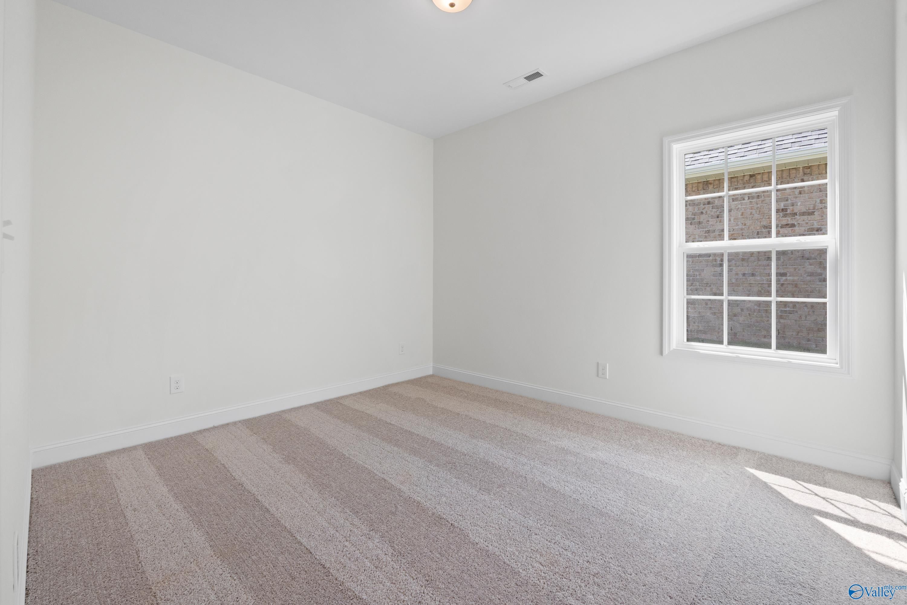 Empty secondary bedroom featuring white walls, large window, and neutral striped carpet in Davidson Homes The Rockford B, Toney, Alabama