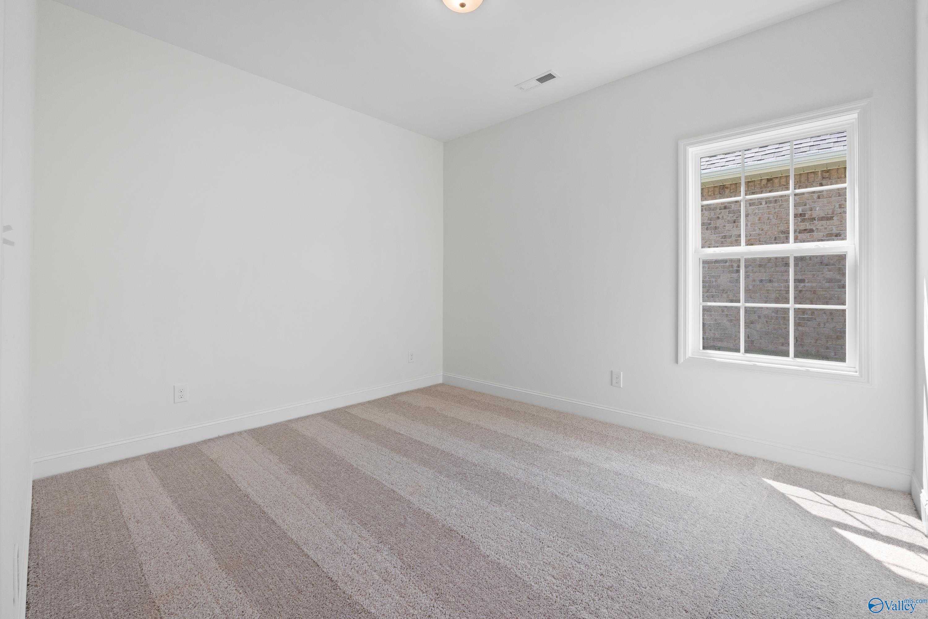 Empty secondary bedroom featuring white walls, large window, and neutral striped carpet in Davidson Homes The Rockford B, Toney, Alabama