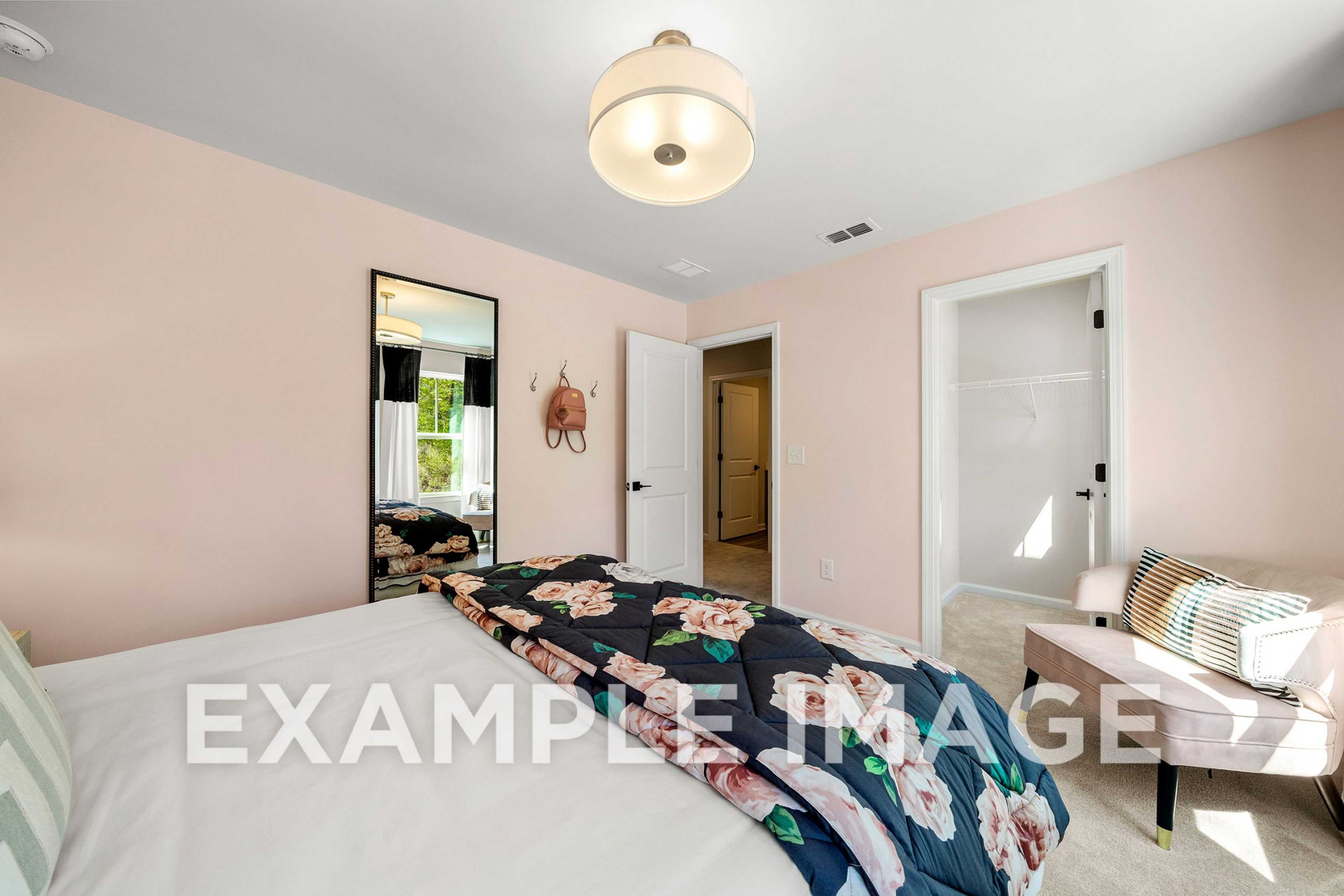 Cozy master bedroom in The Hickory A featuring soft pink walls, floral duvet, tufted bench, and ensuite door