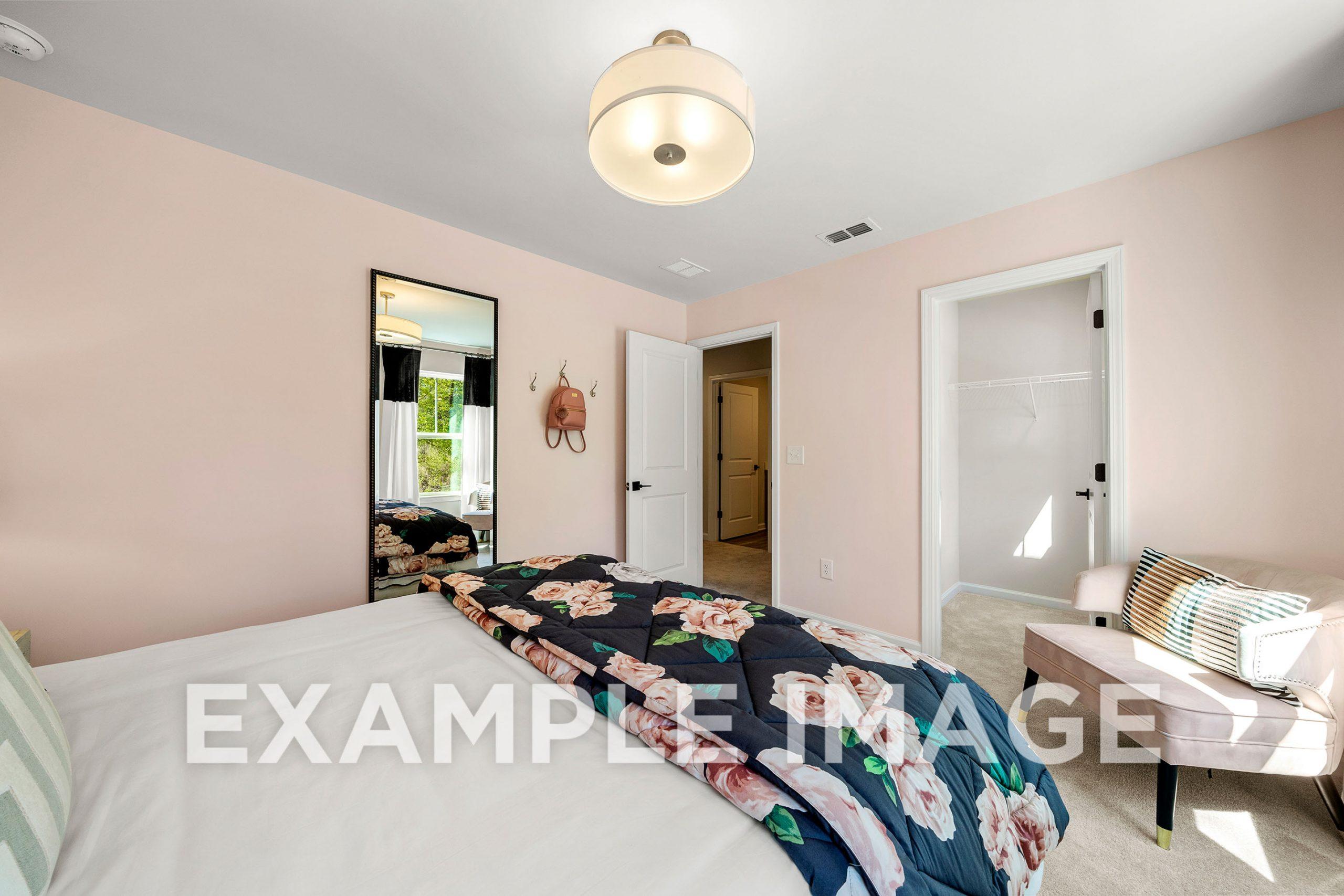 Spacious master bedroom in The Hickory B with floral duvet, pink walls, vanity mirror, and en-suite bathroom door