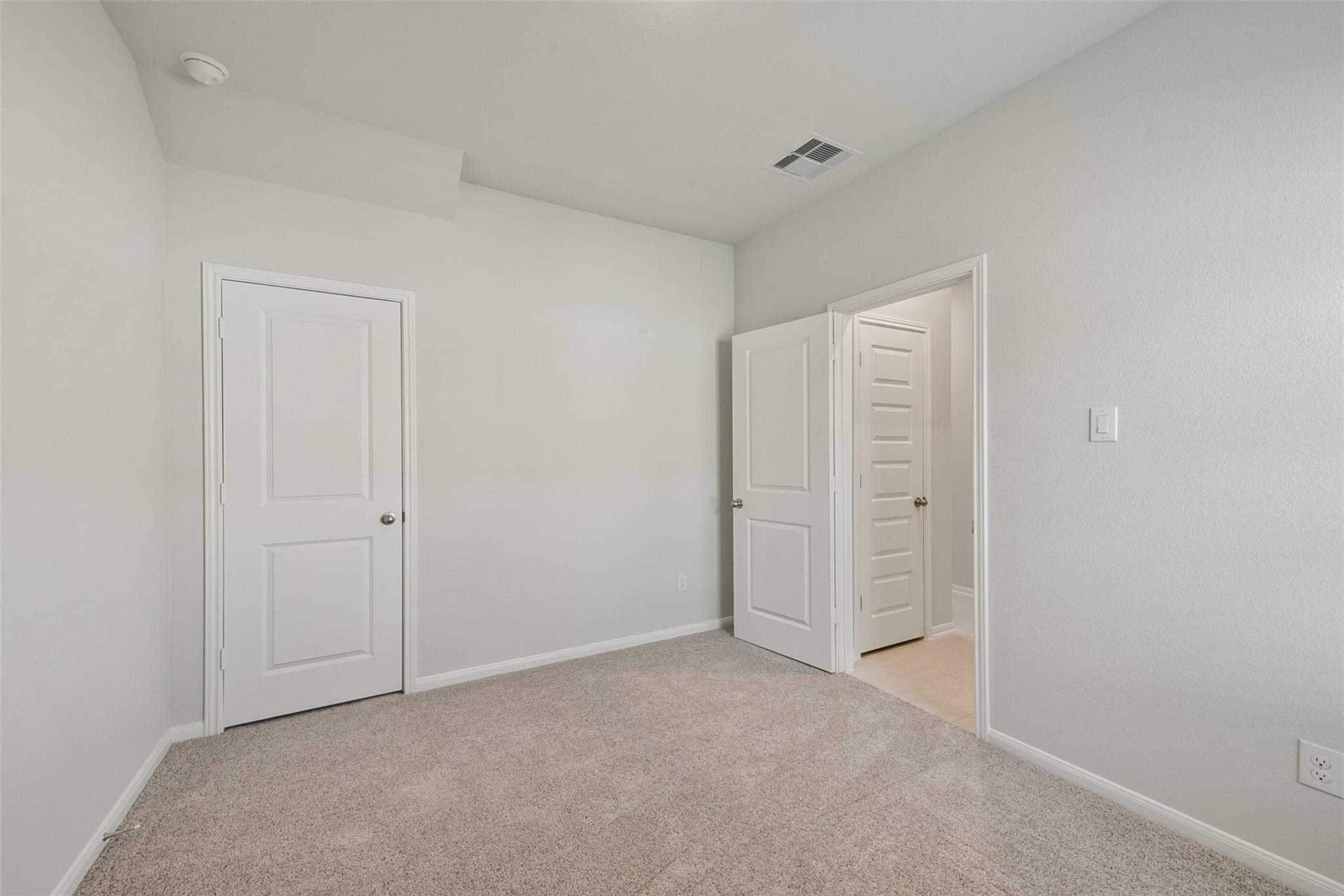 Spacious secondary bedroom with light gray walls, beige carpet, white doors and bathroom access in Davidson Homes Sabine E, Dayton TX