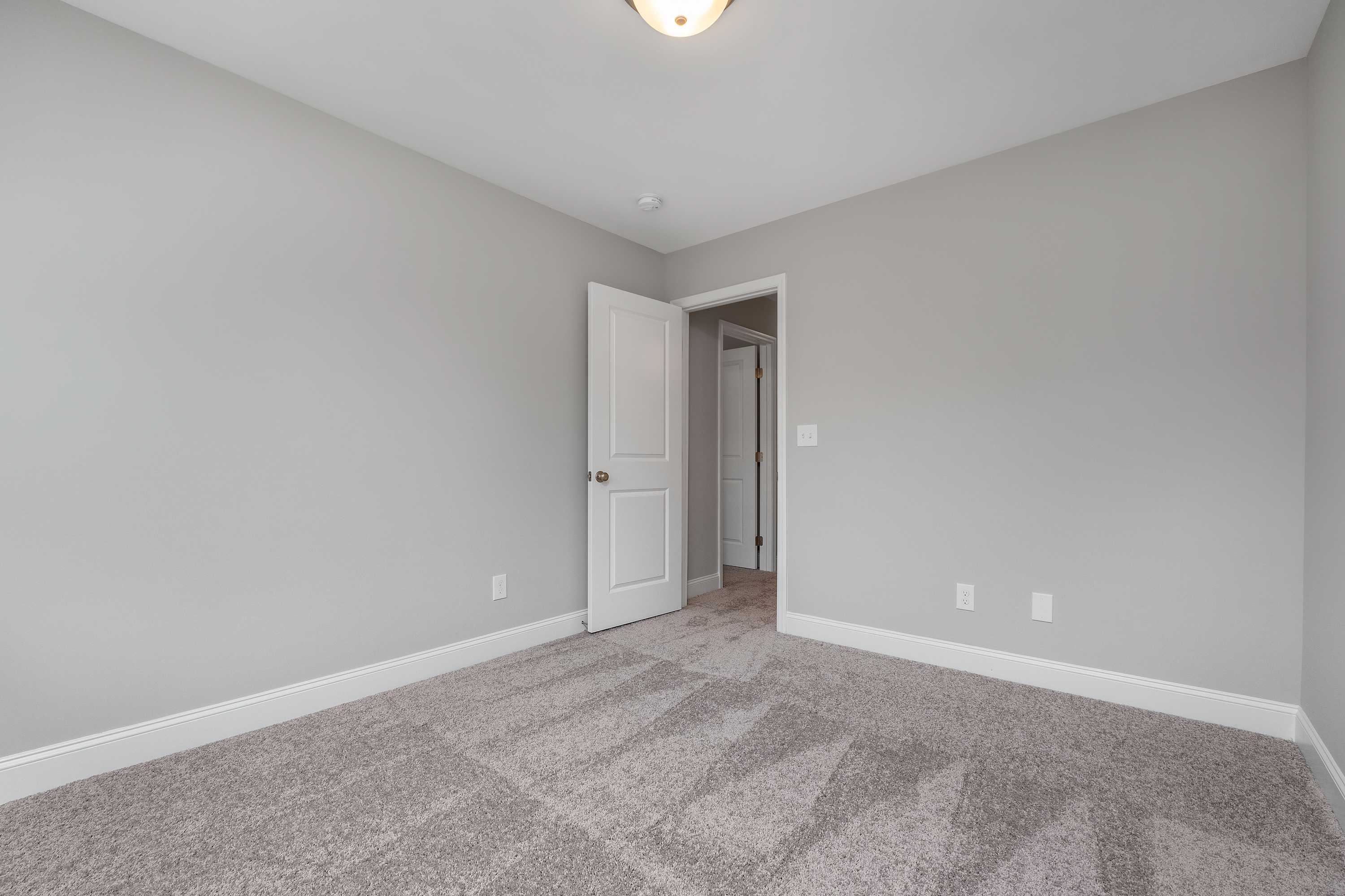 Spacious secondary bedroom in The Aiken with light gray walls, neutral carpet flooring, white door, and ceiling light