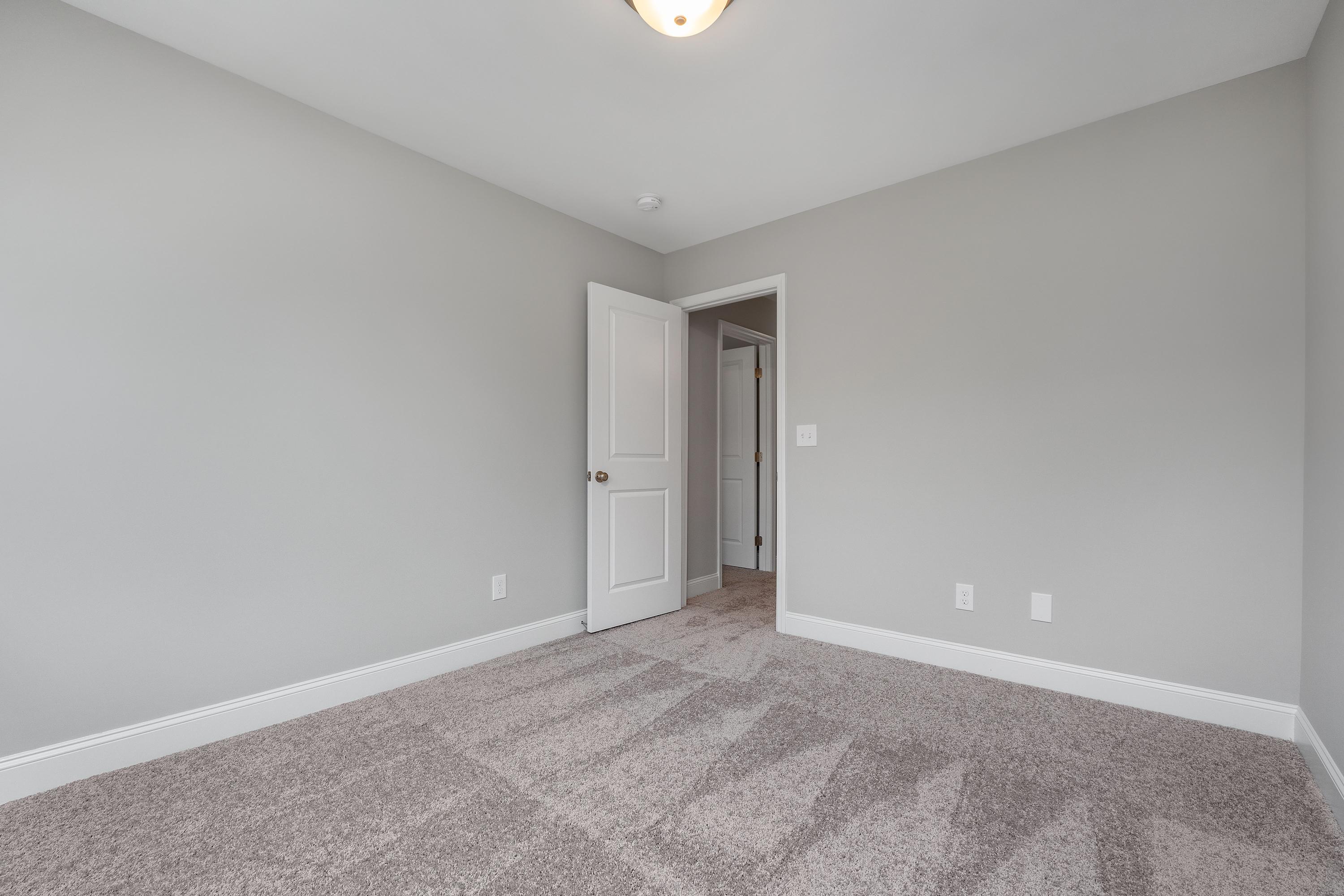 Spacious secondary bedroom in The Aiken with light gray walls, neutral carpet flooring, white door, and ceiling light