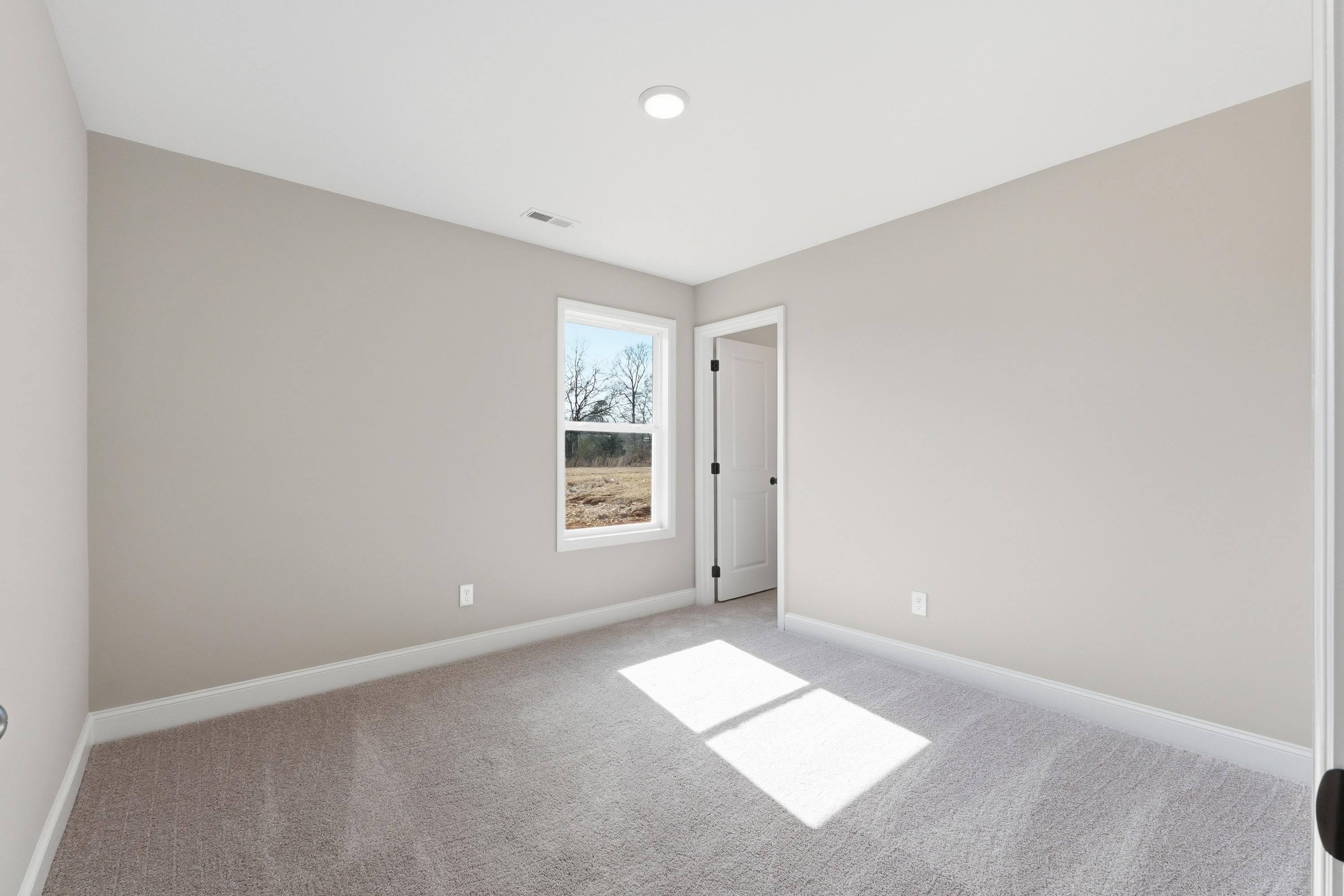 Spacious secondary bedroom in The Daphne V with light gray walls, beige carpet, large window and natural sunlight