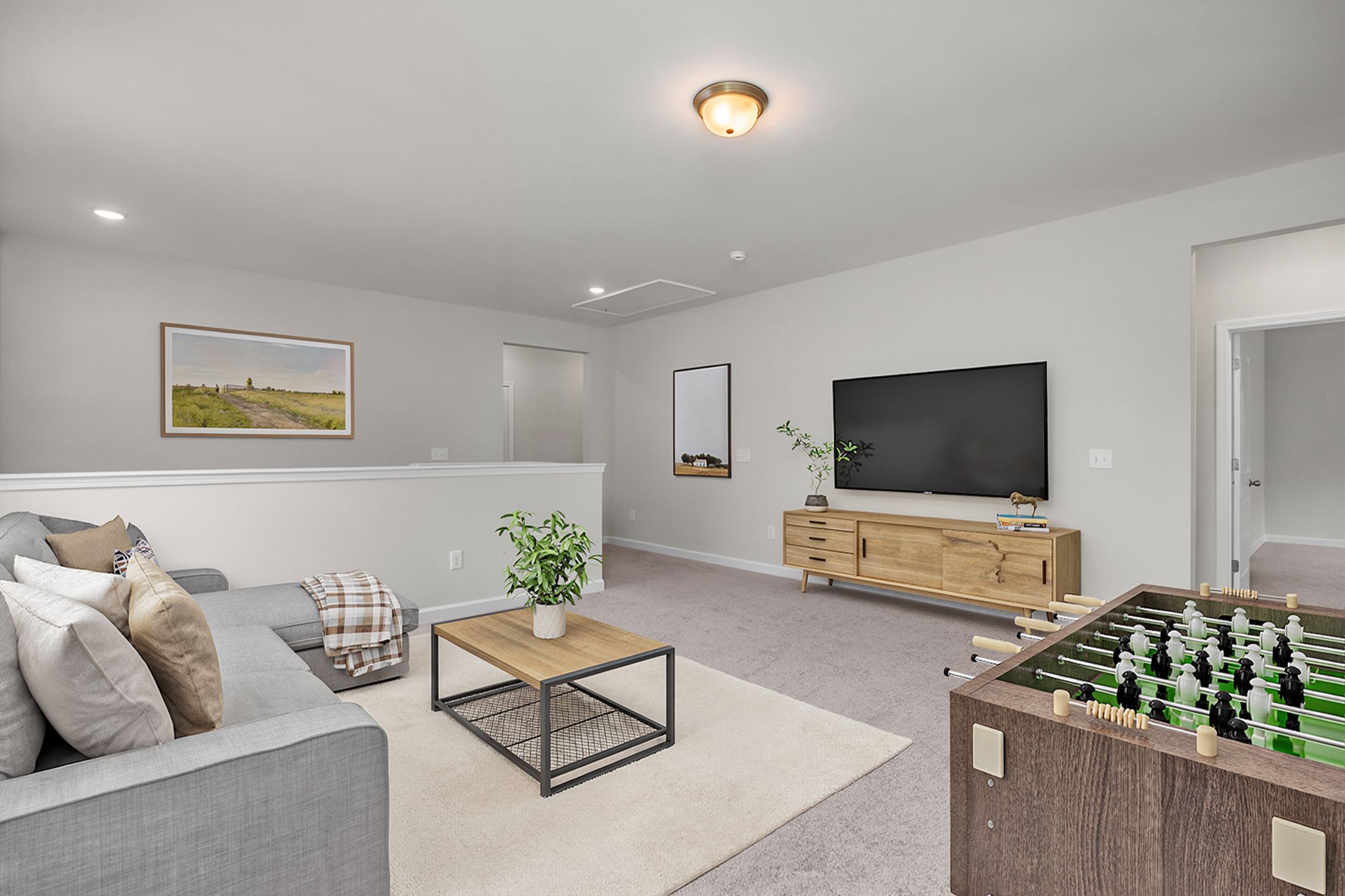 Spacious bonus room at Windgate in Mooresville NC with gray sectional sofa, foosball table, TV console, plants and modern decor by Davidson Homes