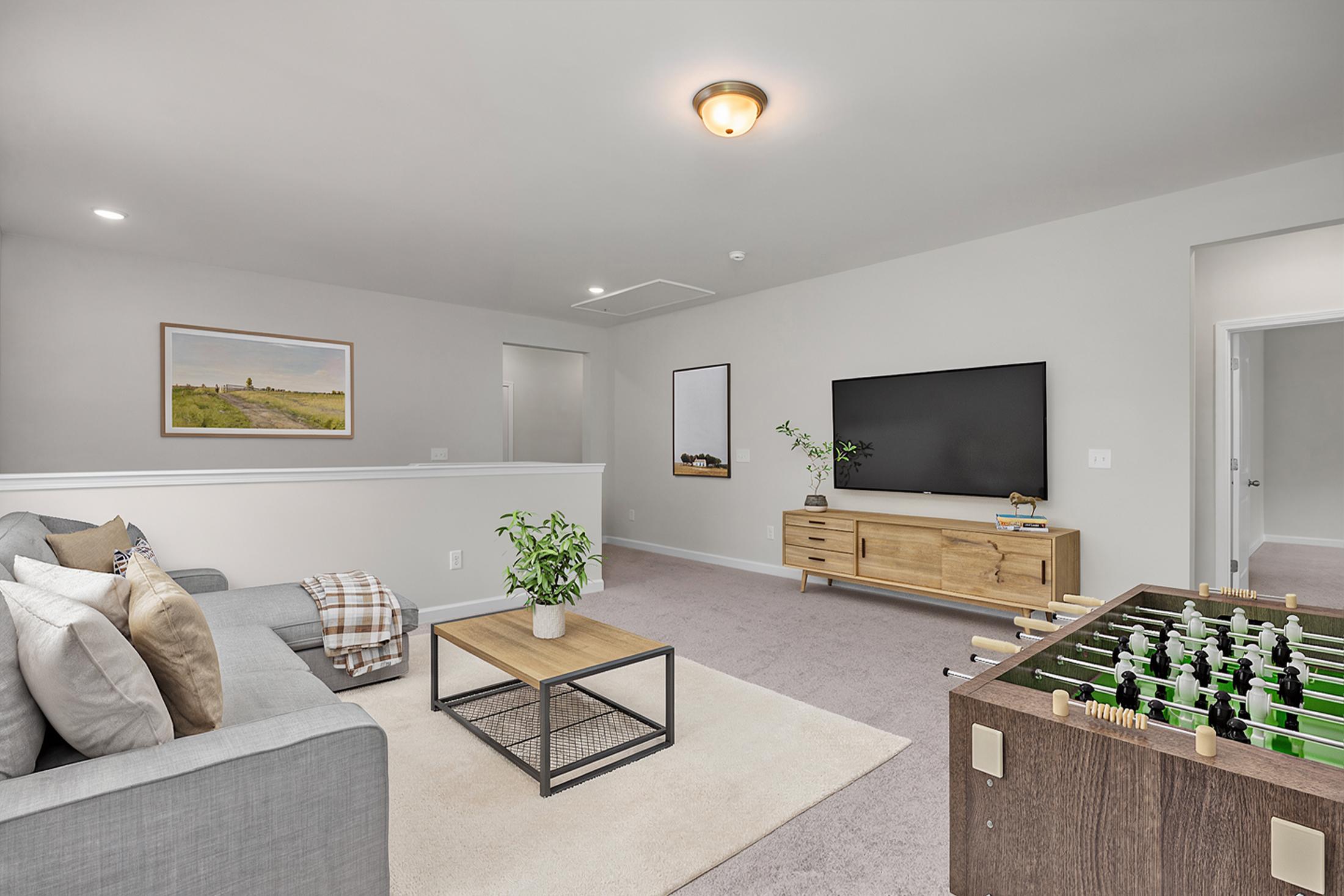 Spacious bonus room at Windgate in Mooresville NC with gray sectional sofa, foosball table, TV console, plants and modern decor by Davidson Homes