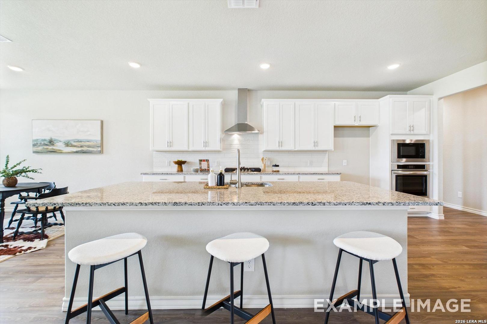 Modern kitchen with granite island and white cabinets in The Foster F floor plan by Davidson Homes, Castroville, Texas.