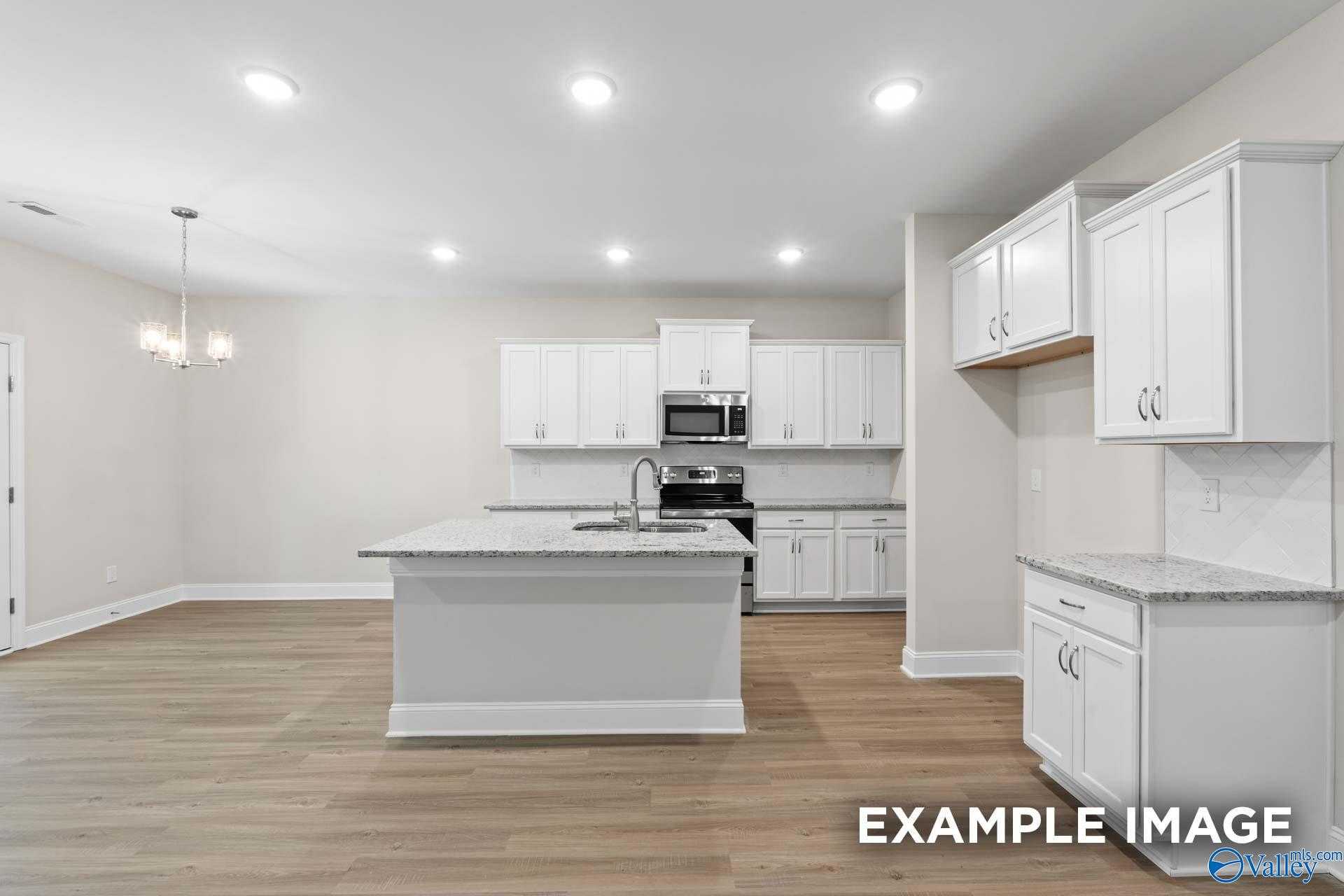 Modern white kitchen featuring large granite island, stainless steel appliances, and recessed lighting in The Camden C floor plan, Huntsville AL