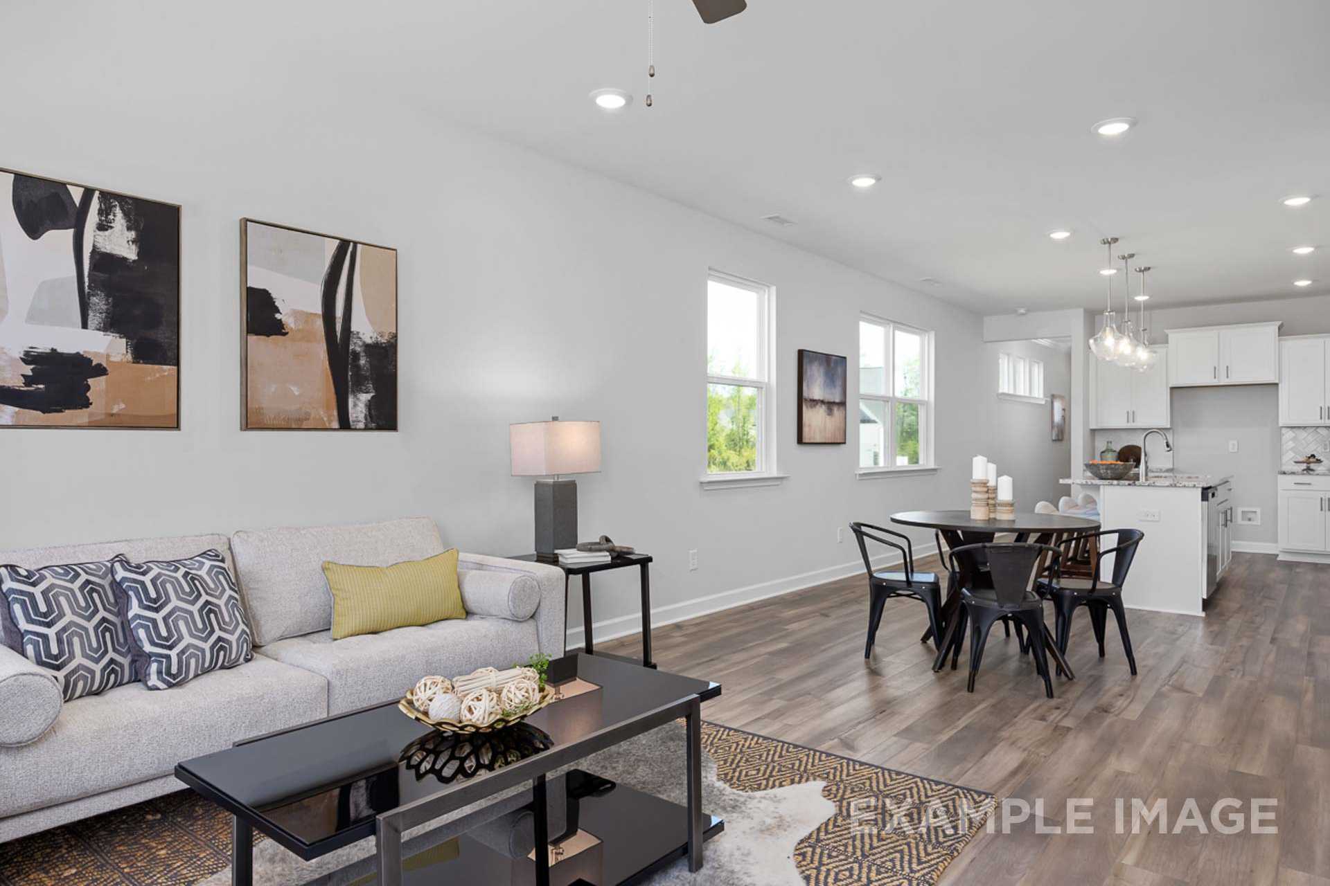 Open-concept living and dining area in The Carter B by Davidson Homes, Lillington NC, featuring gray sofa, modern art, and white kitchen