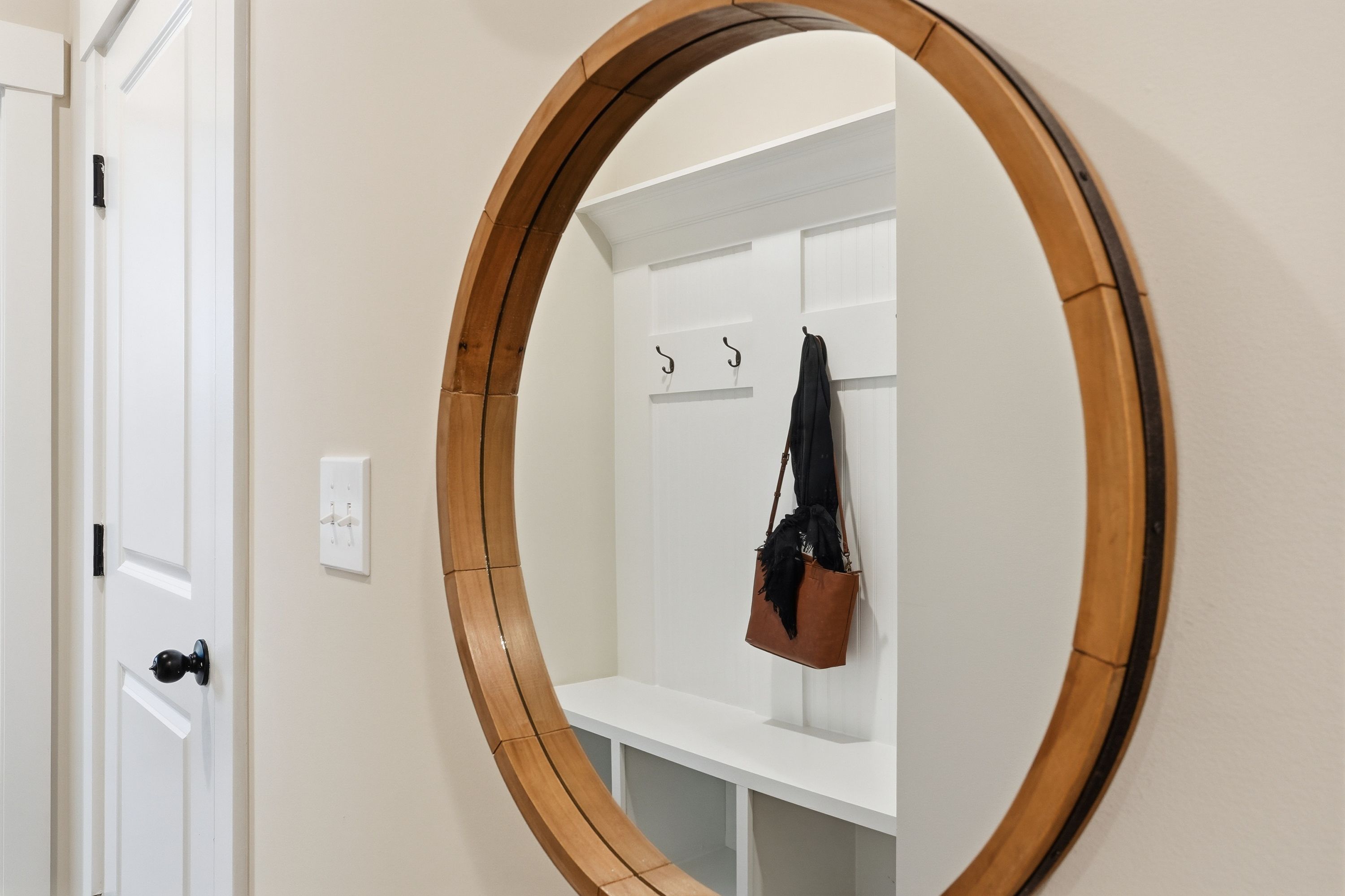 Round wooden mirror above white built-in coat hooks and bench in entryway at Noble Ridge Cullman Alabama