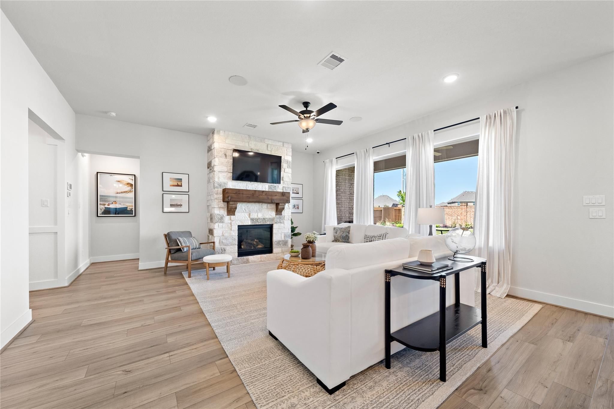 Bright living room with stone fireplace, white sofa, and wood-look tile floors in Davidson Homes The Edward A, Lago Mar, Texas City