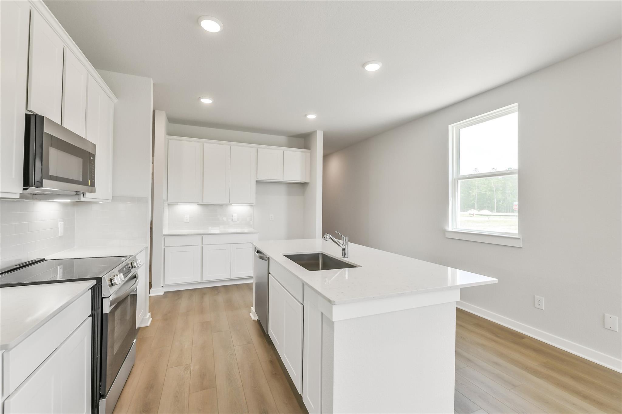 Modern white kitchen with quartz island sink, stainless steel appliances, subway tile backsplash in Davidson Homes The Frio G, Conroe, TX