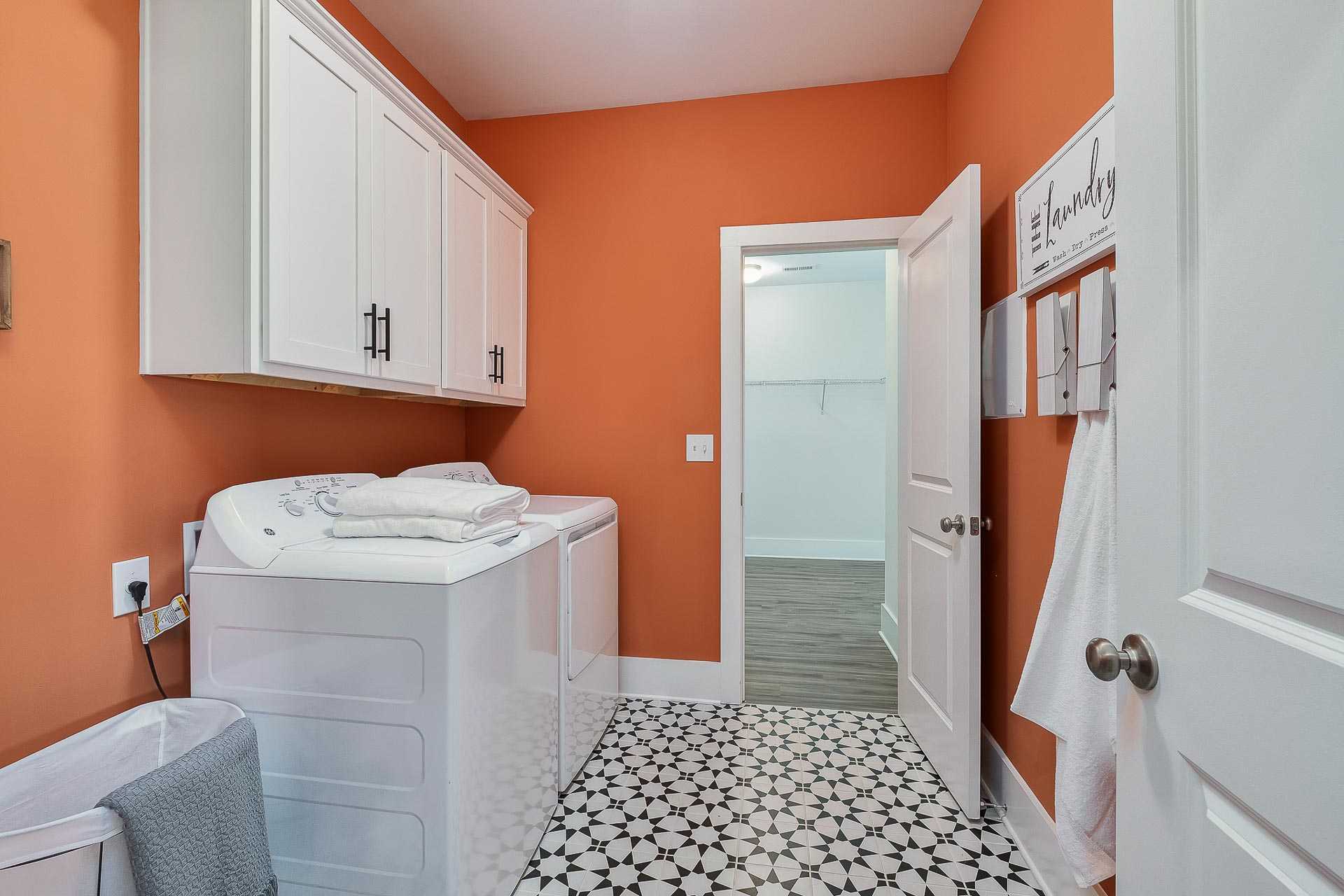 Modern laundry room at Newby Chapel in Athens Alabama with orange walls white cabinets stacked washer dryer and star-patterned tile floor