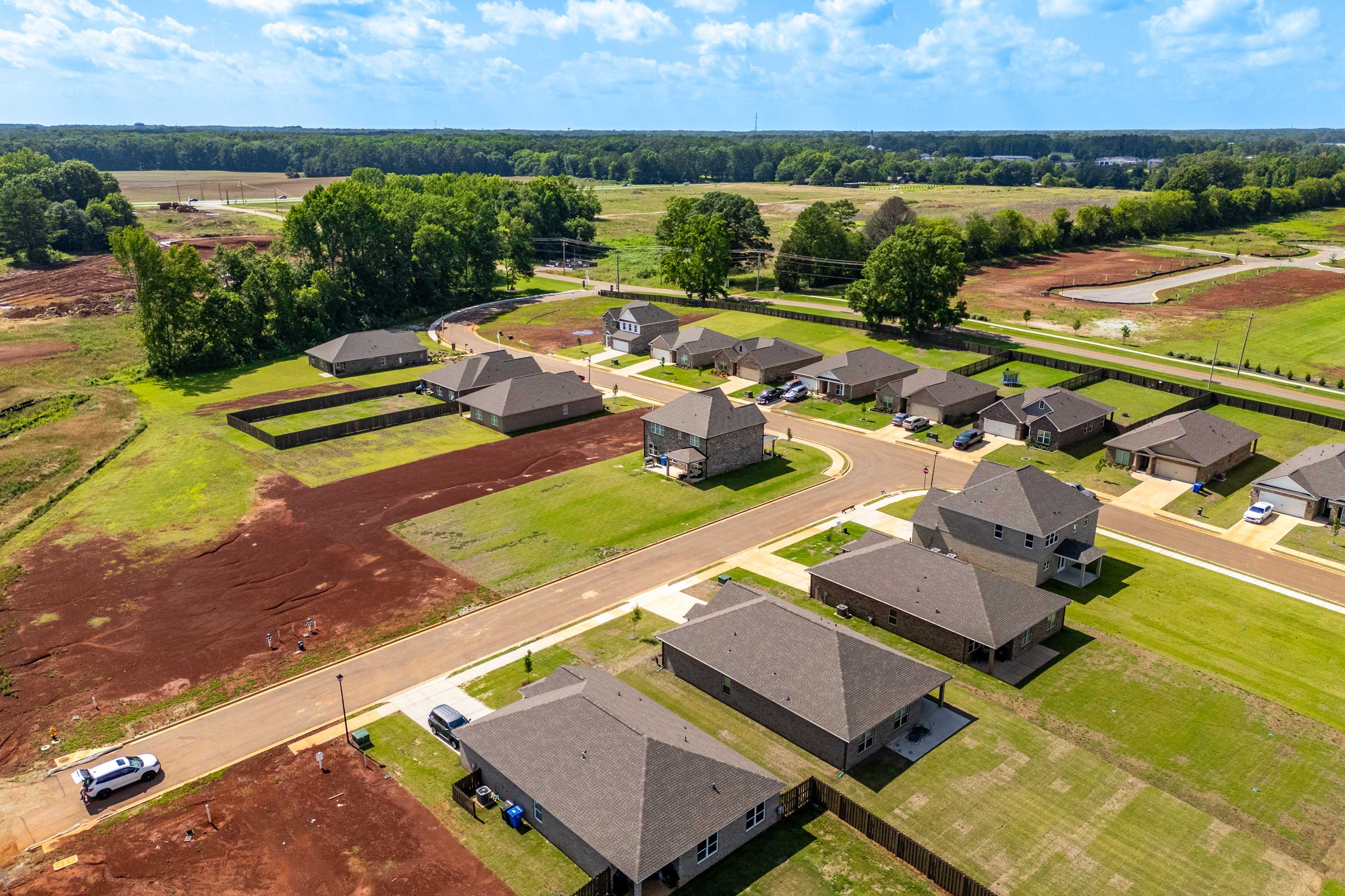 Aerial view of new brick homes in The Meadows, Athens Alabama surrounded by green lawns, woods and construction sites