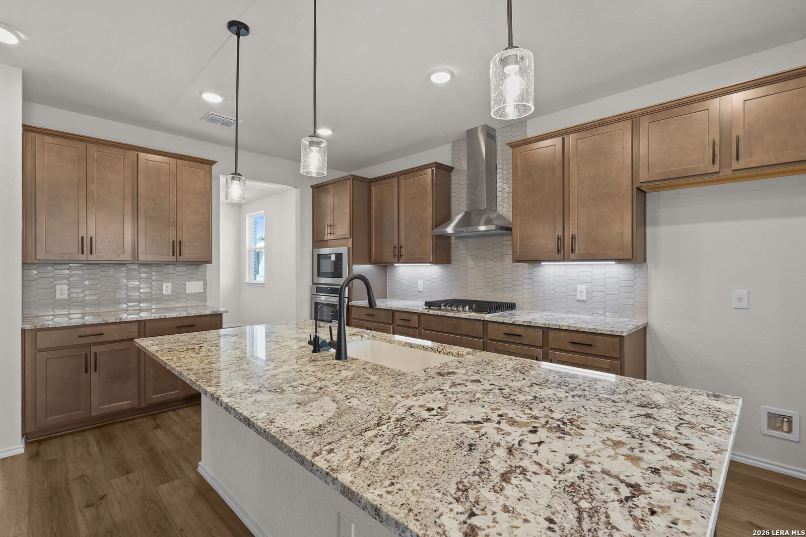 Kitchen island with granite countertops, pendant lights, and wood cabinets in The Glenwood E floor plan at Comanche Ridge, San Antonio