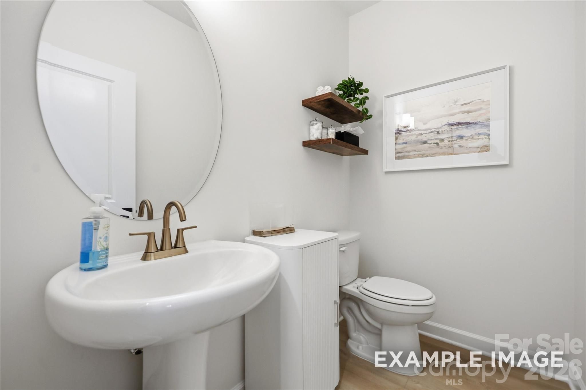 Elegant powder room with pedestal sink, gold faucet, round mirror, and wood floating shelves in Davidson Homes Aspen B, Mooresville NC